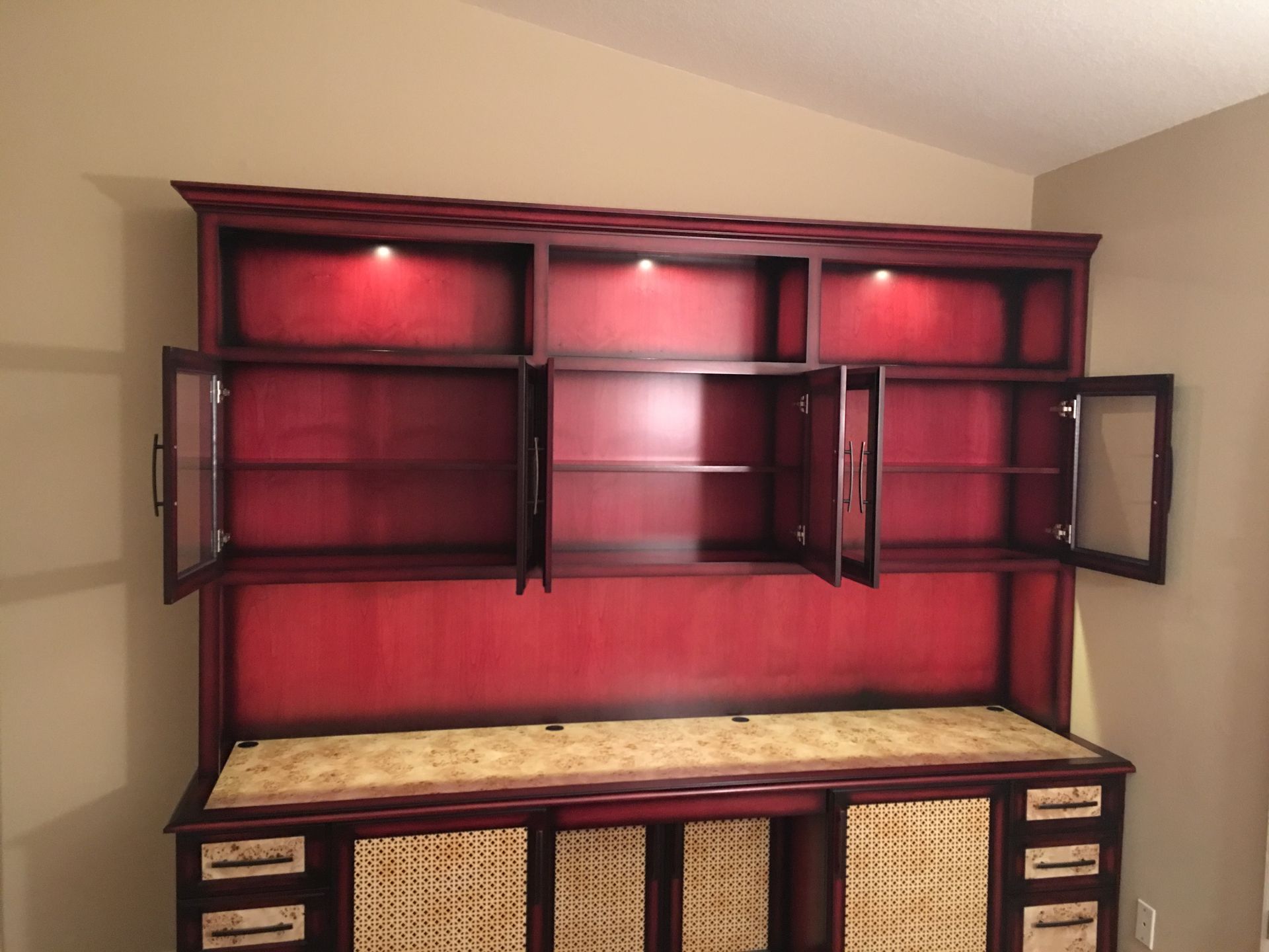 Red wooden hutch with open glass-doored cabinets and interior lighting above a desk with woven panels.