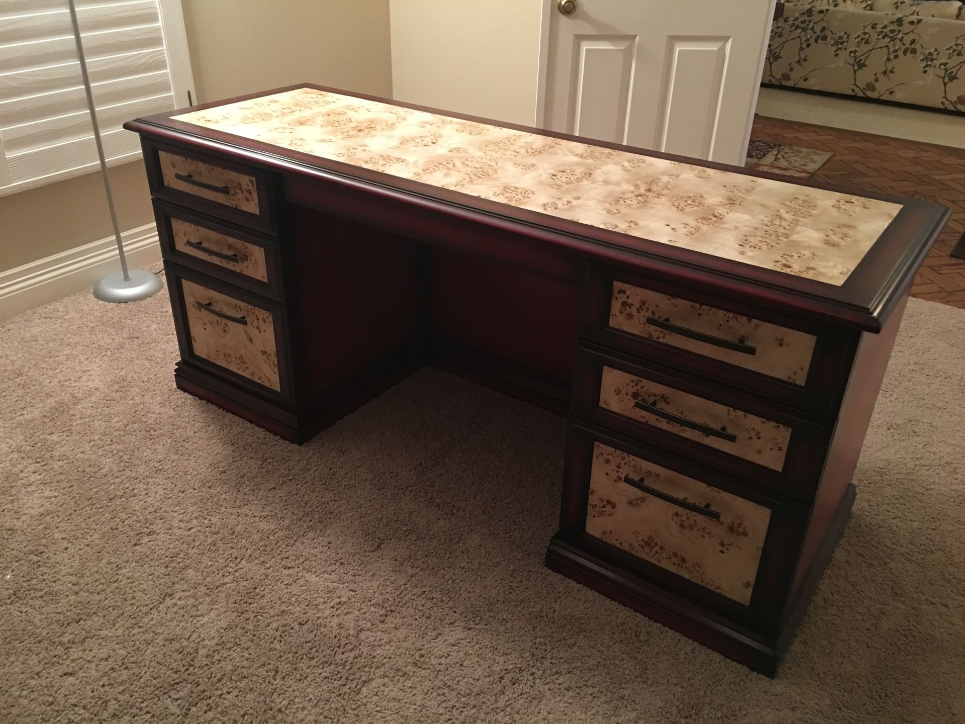 Dark wood desk with a patterned top and drawer panels on a carpeted floor.