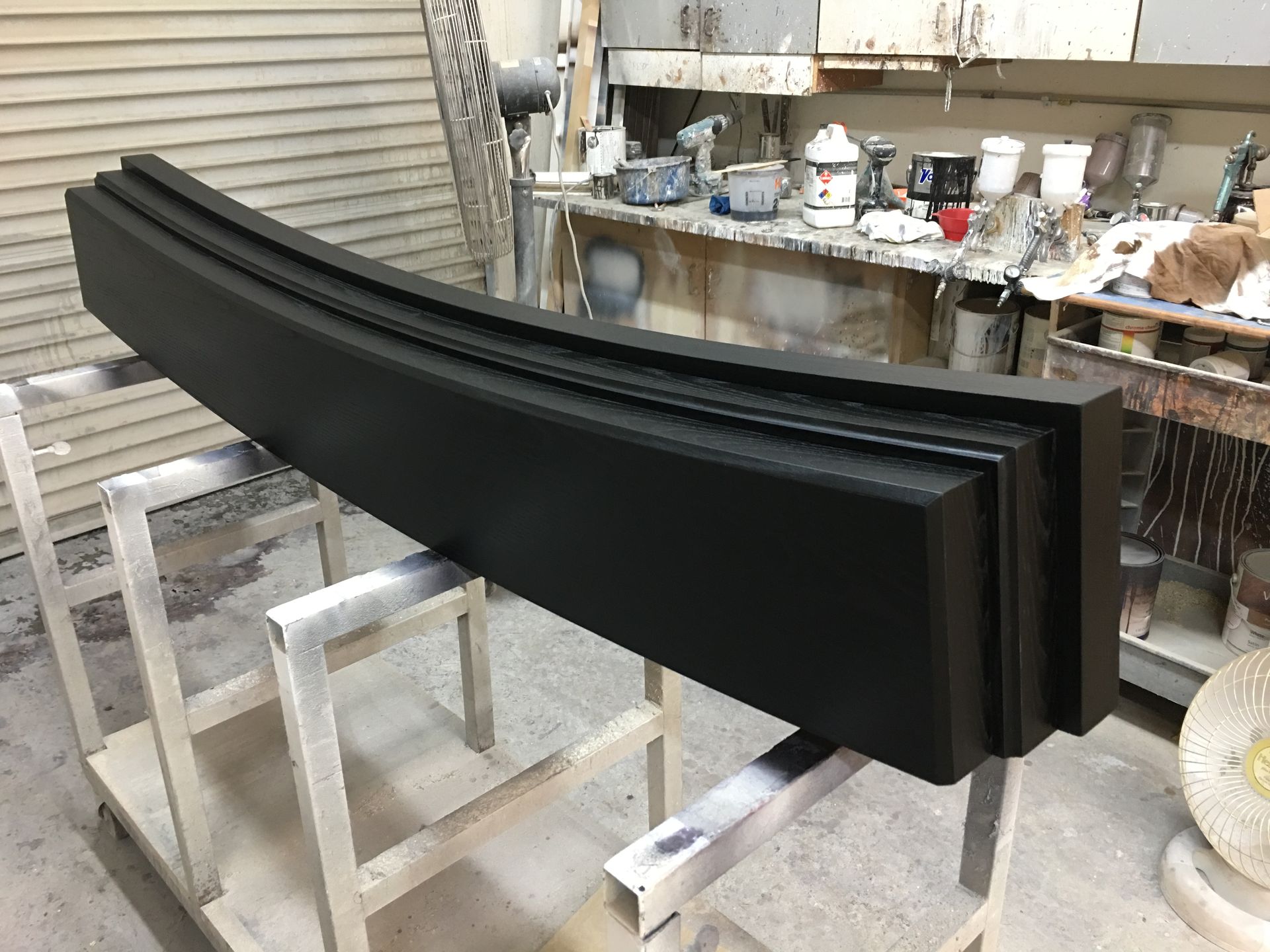 Black, curved architectural molding on a paint stand, in a workshop.