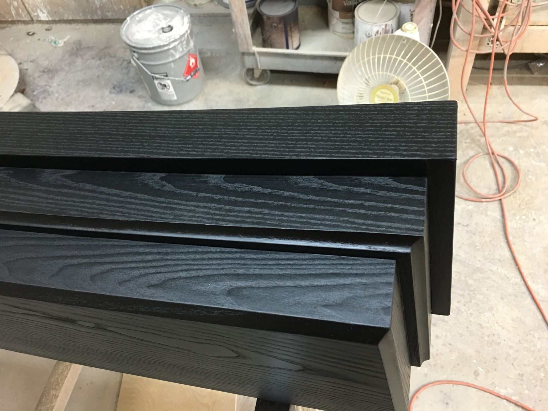 Black painted wooden trim pieces, varying in size and design, on a workbench.