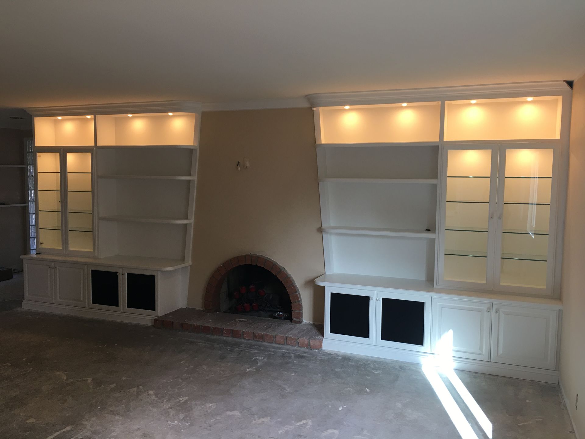 Built-in white bookshelves with upper lighting flanking a brick fireplace in a room.