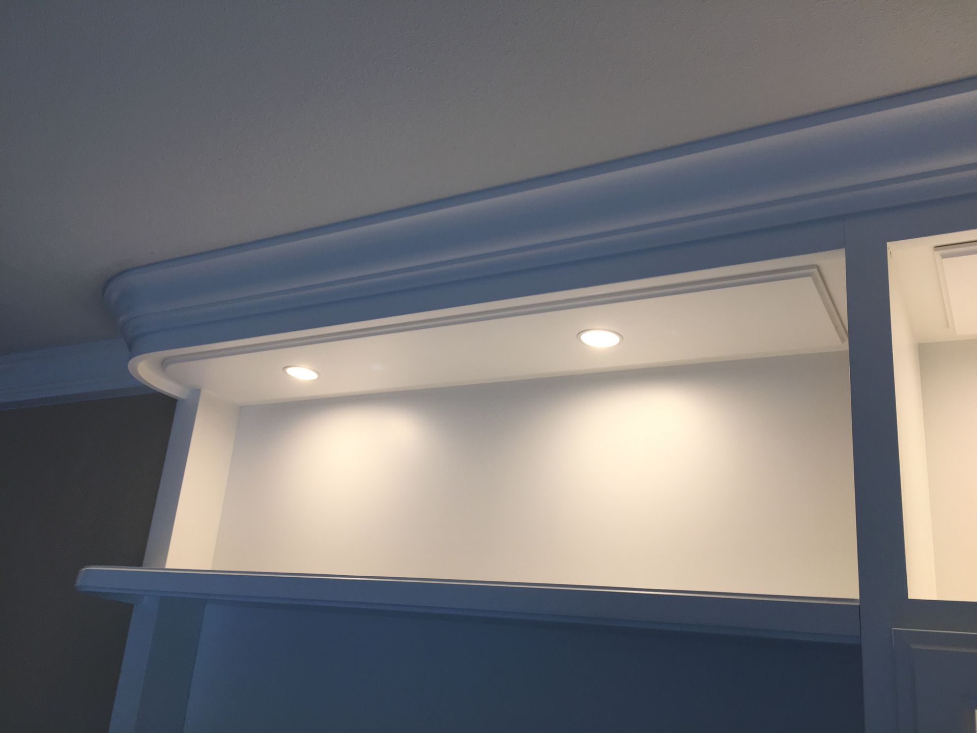 White built-in shelving with recessed lighting under crown molding.