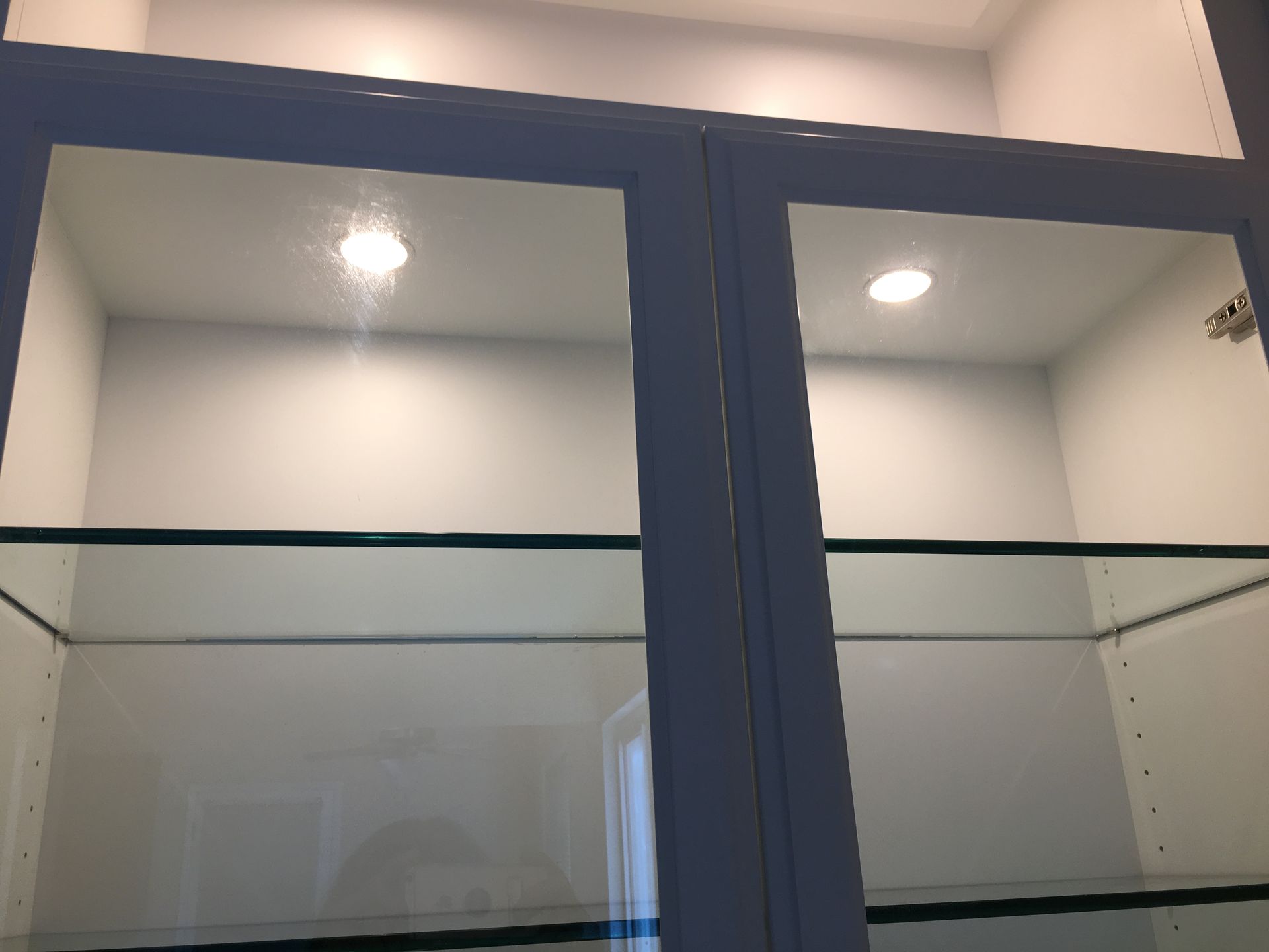 Glass-doored white cabinet with two recessed lights, two glass shelves.