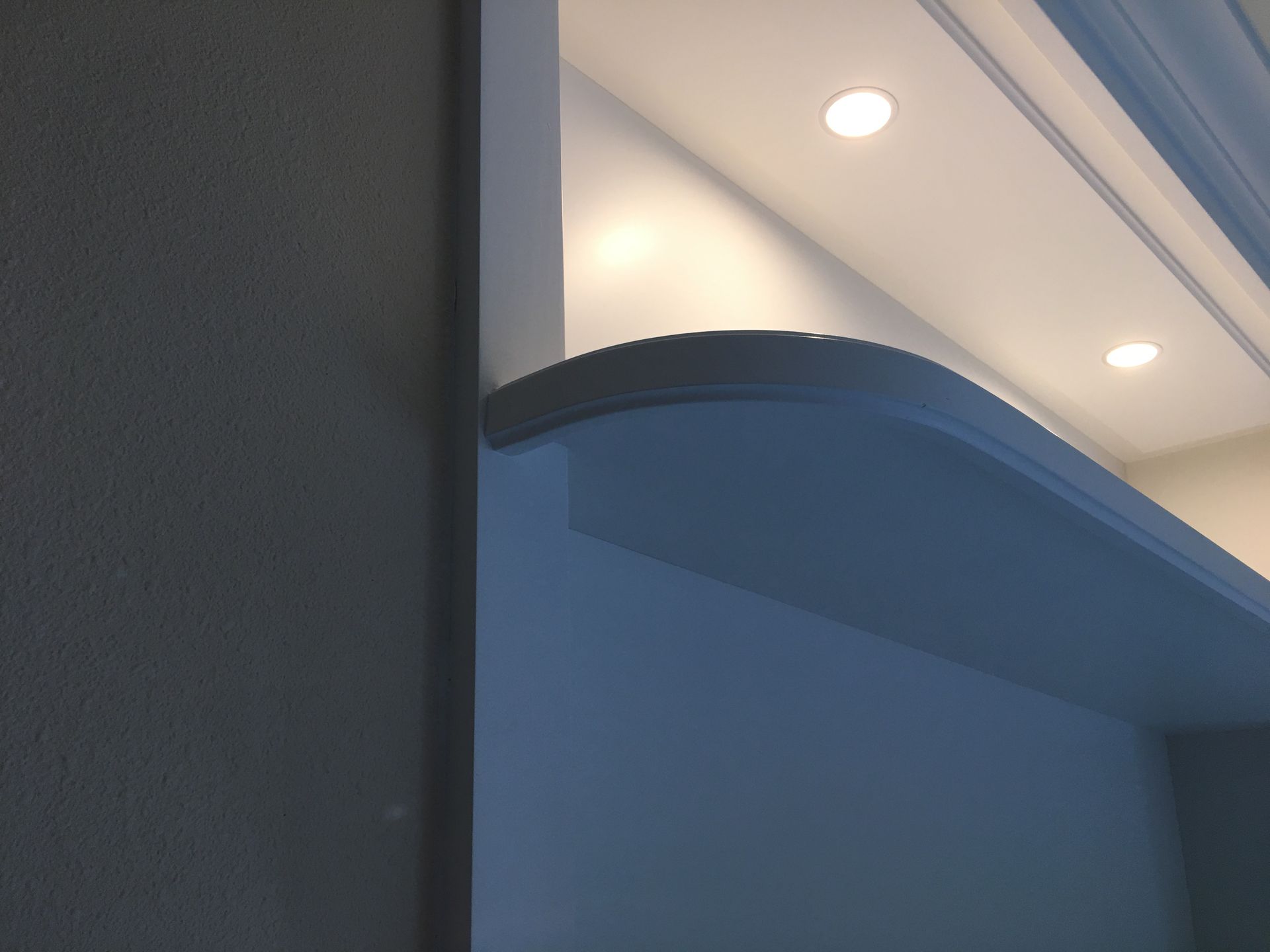 Curved shelf with recessed lighting, painted white and gray, near a wall.