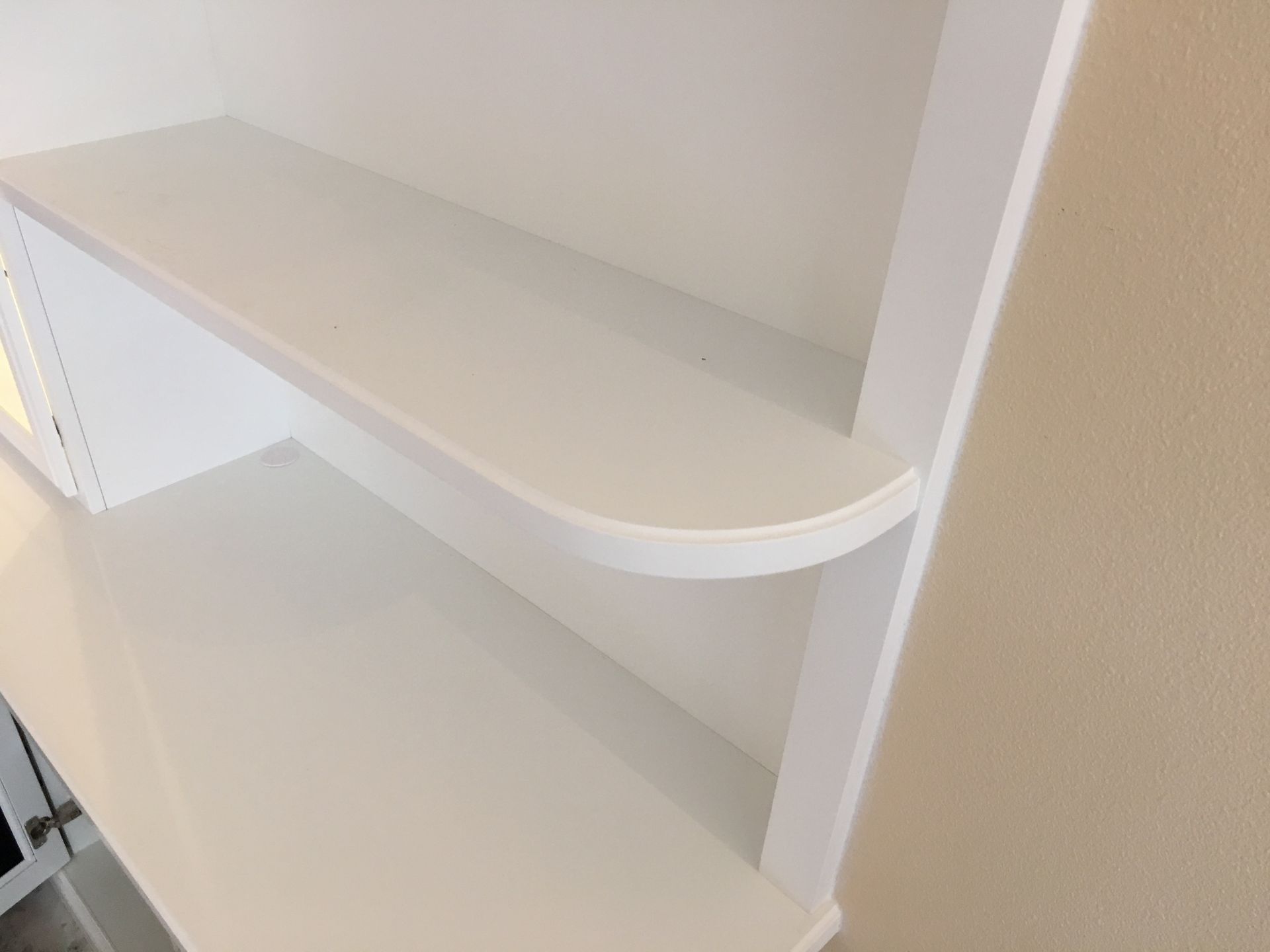 White built-in shelves with a rounded edge, against a cream-colored wall.