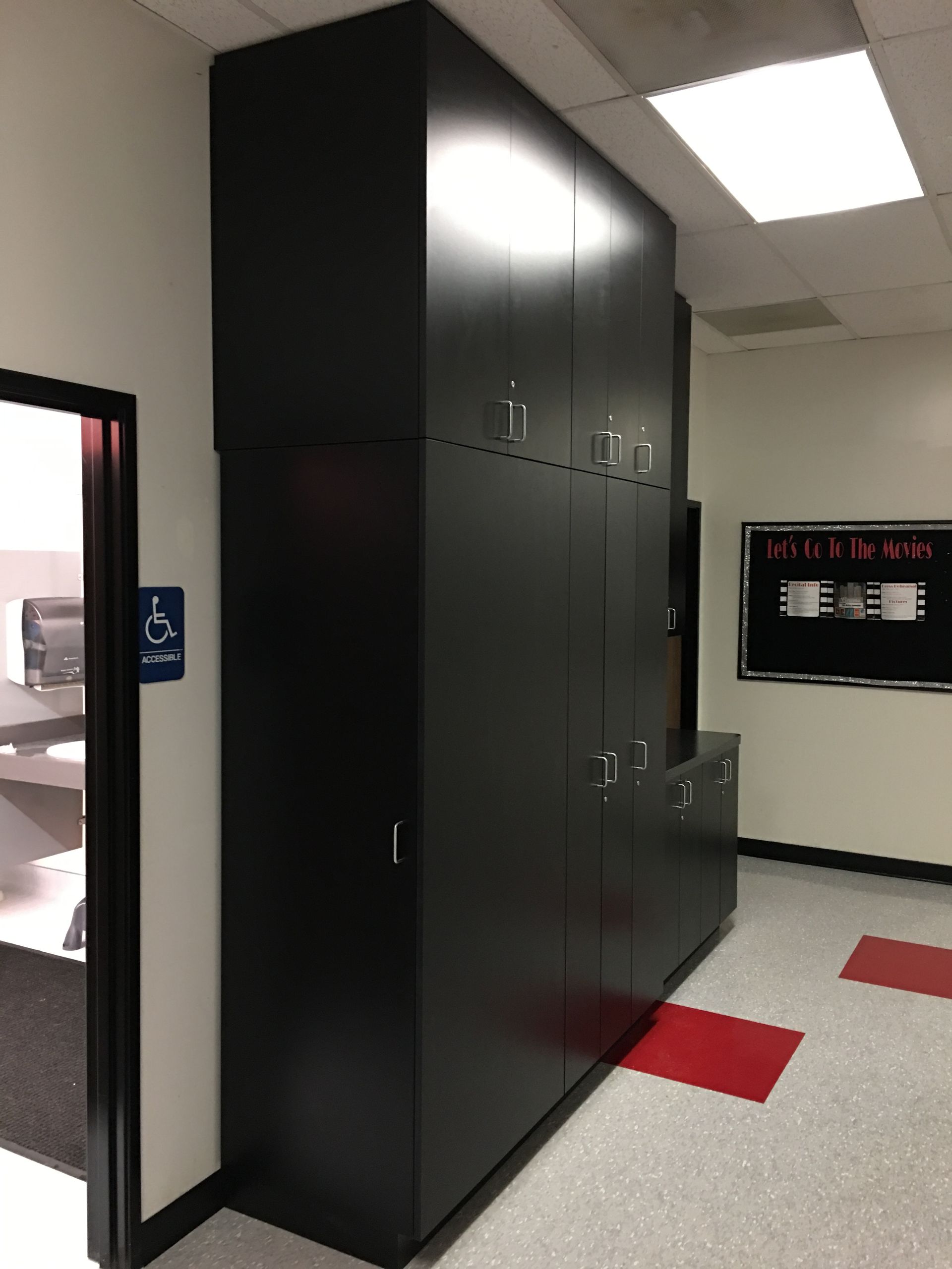Tall black storage cabinets in a hallway. A door and a sign are to the left, and a sign is to the right.
