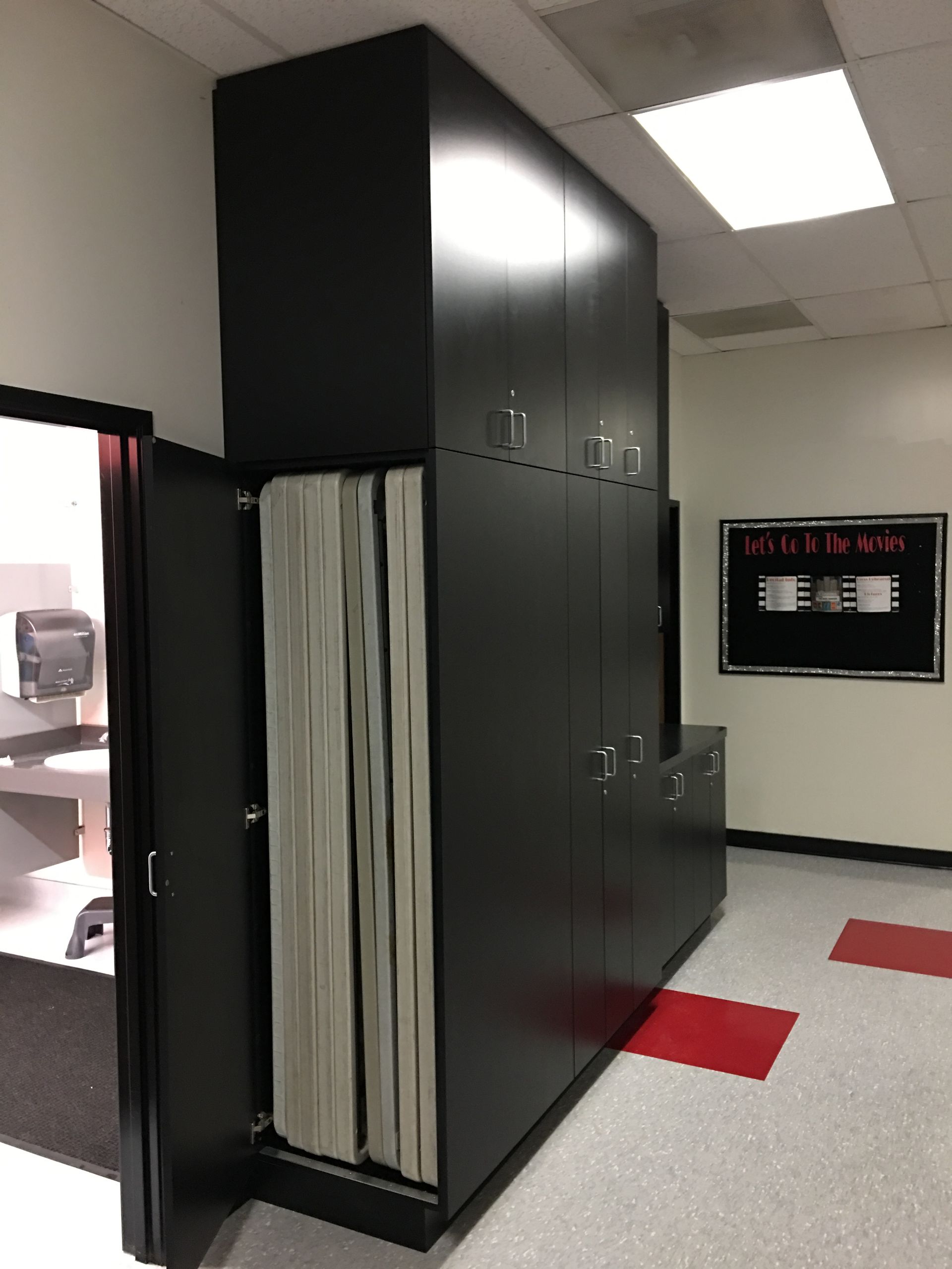 Black filing cabinets in an office hallway, open door revealing hanging files. Red and white tiled floor.