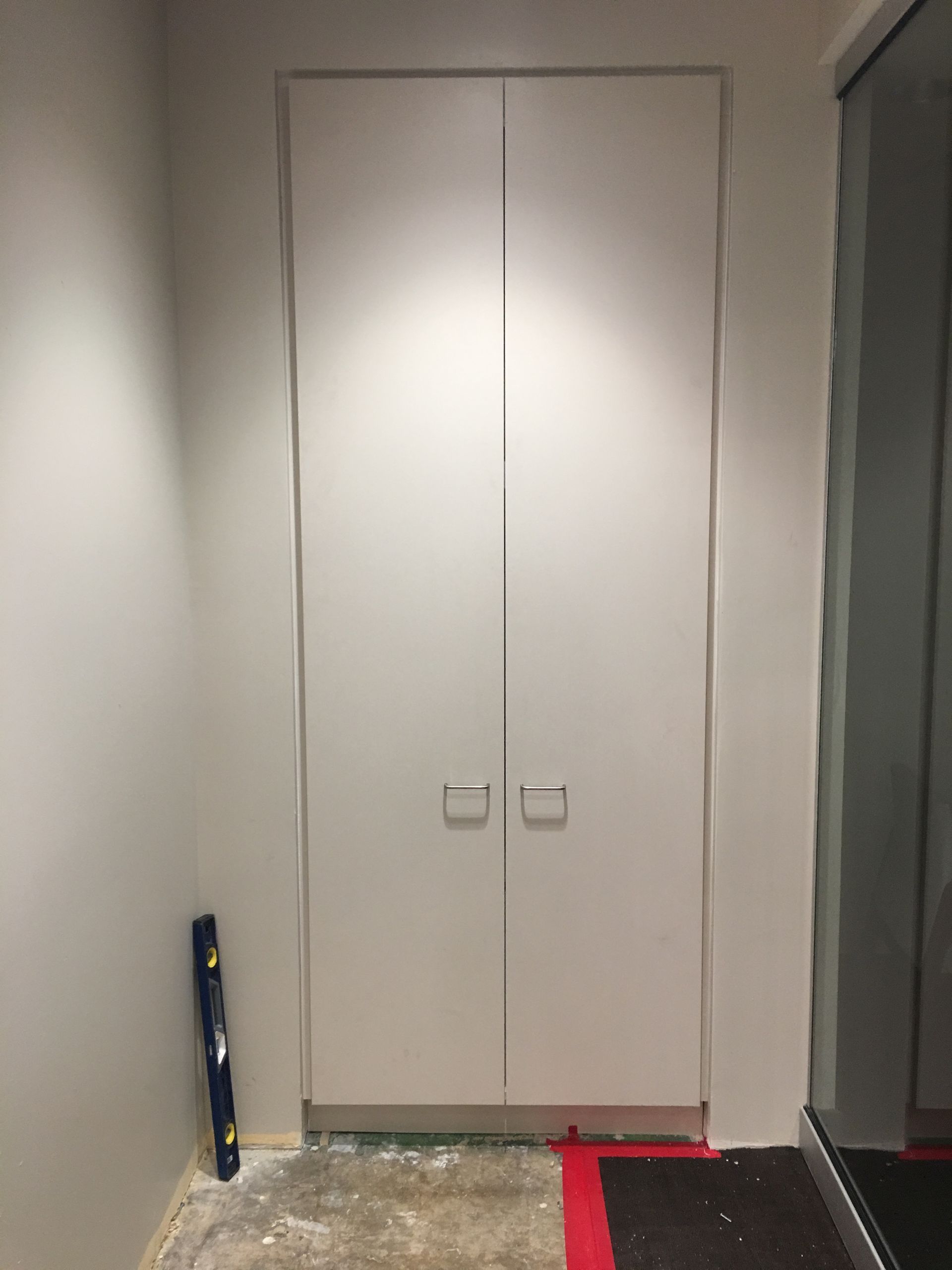 Closed, white double doors in a white wall with a level on the floor.