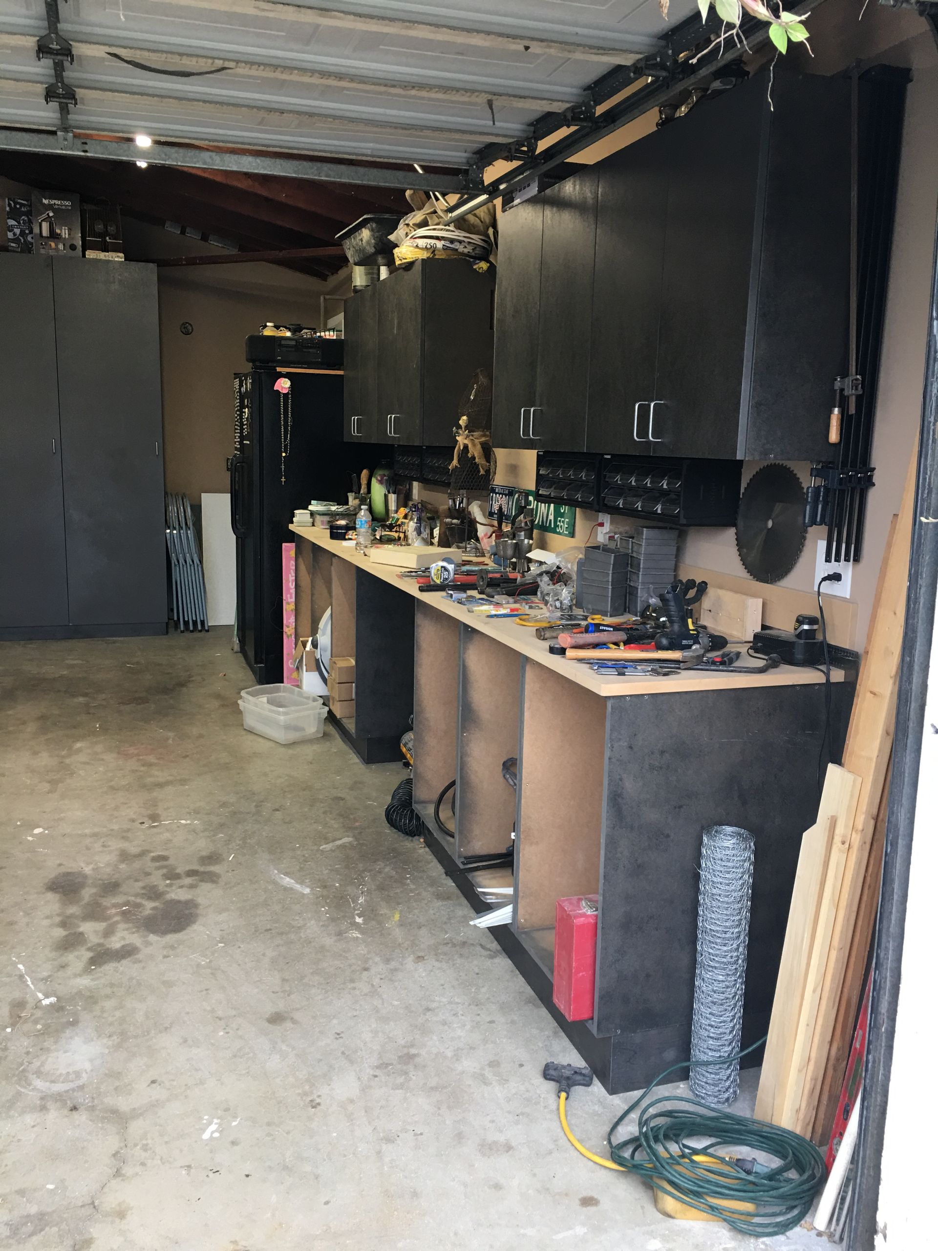 Garage workshop with black cabinets, cluttered workbench, and open garage door.