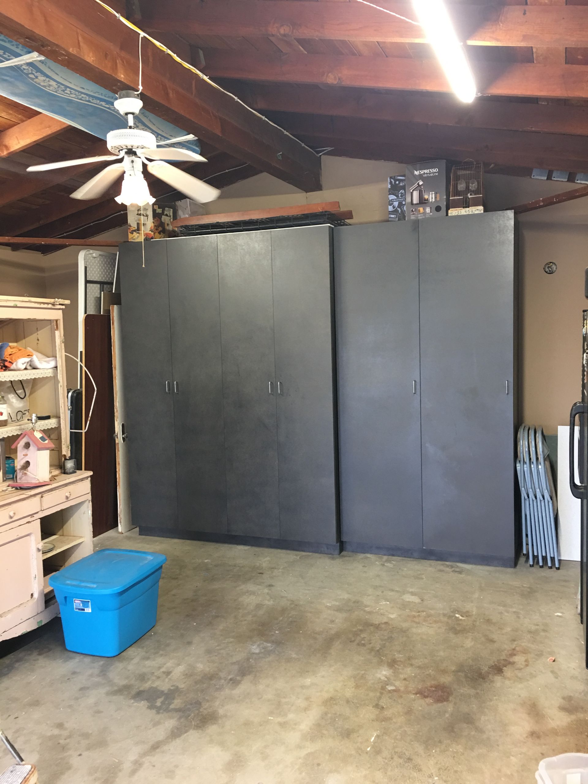 Garage interior with large black cabinets, blue storage bin, and a ceiling fan.