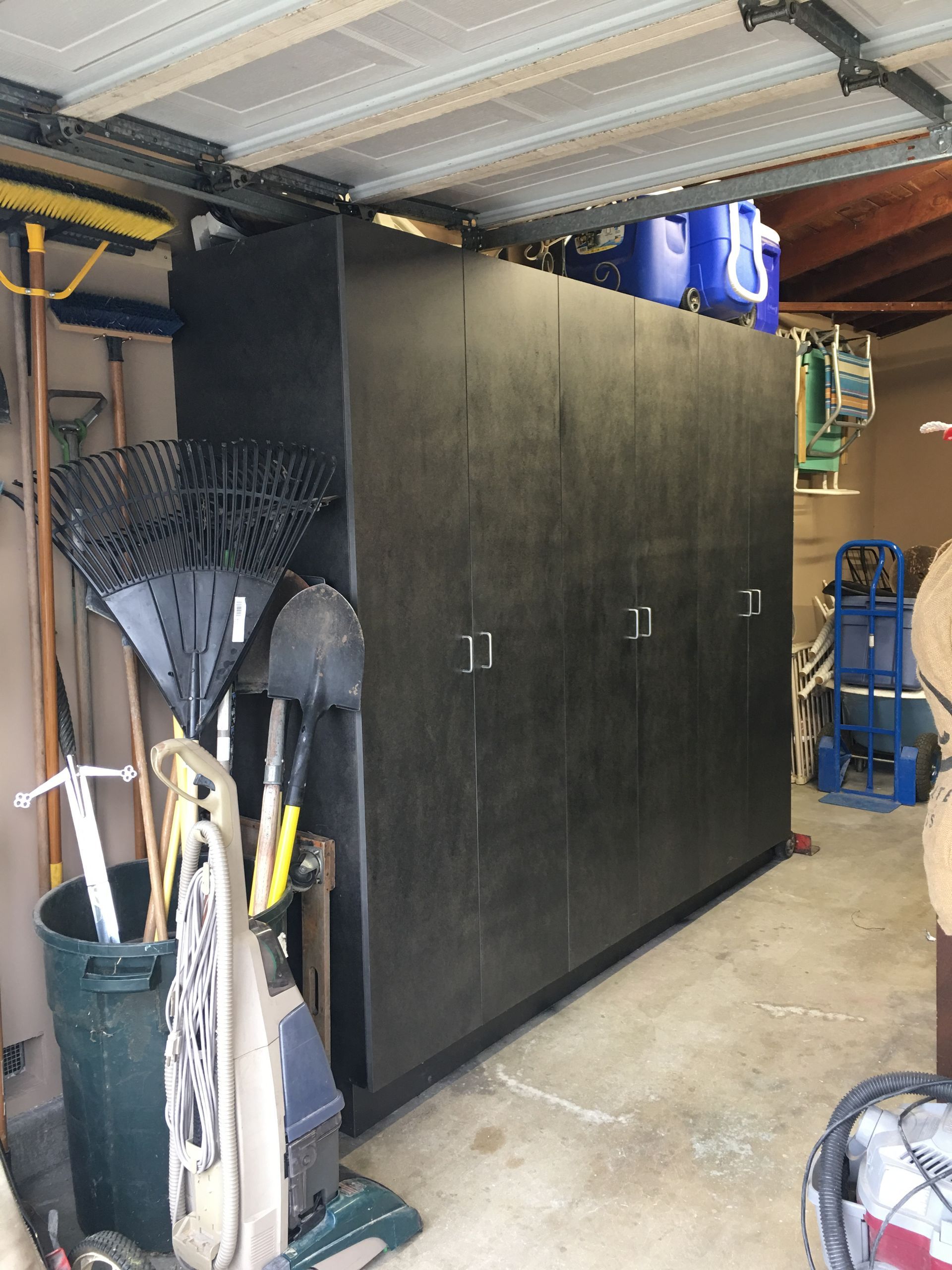 Black storage cabinets in a garage, next to tools and equipment.