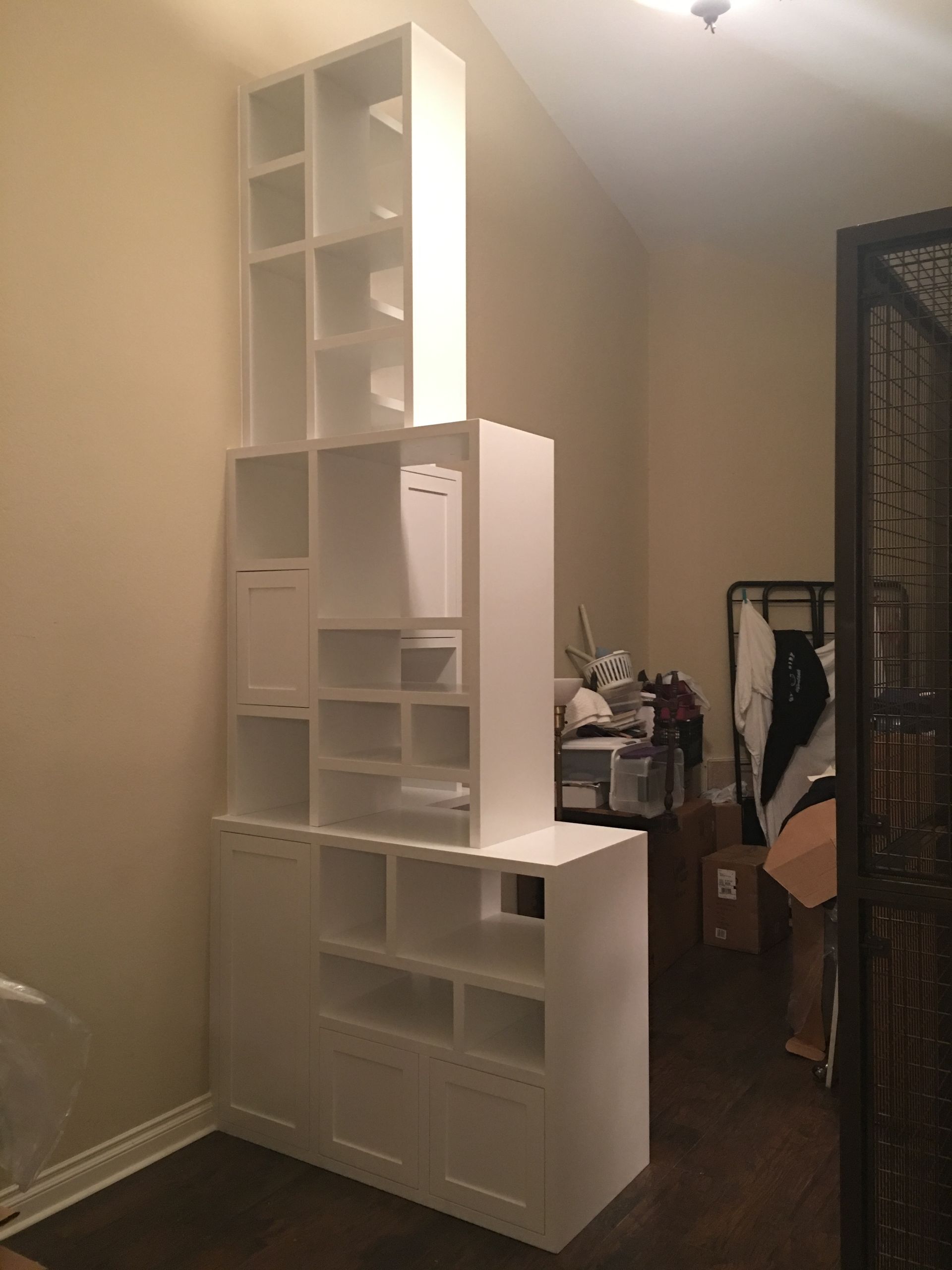 White storage unit with shelves and compartments in a room. Dark wood floor and light brown walls.