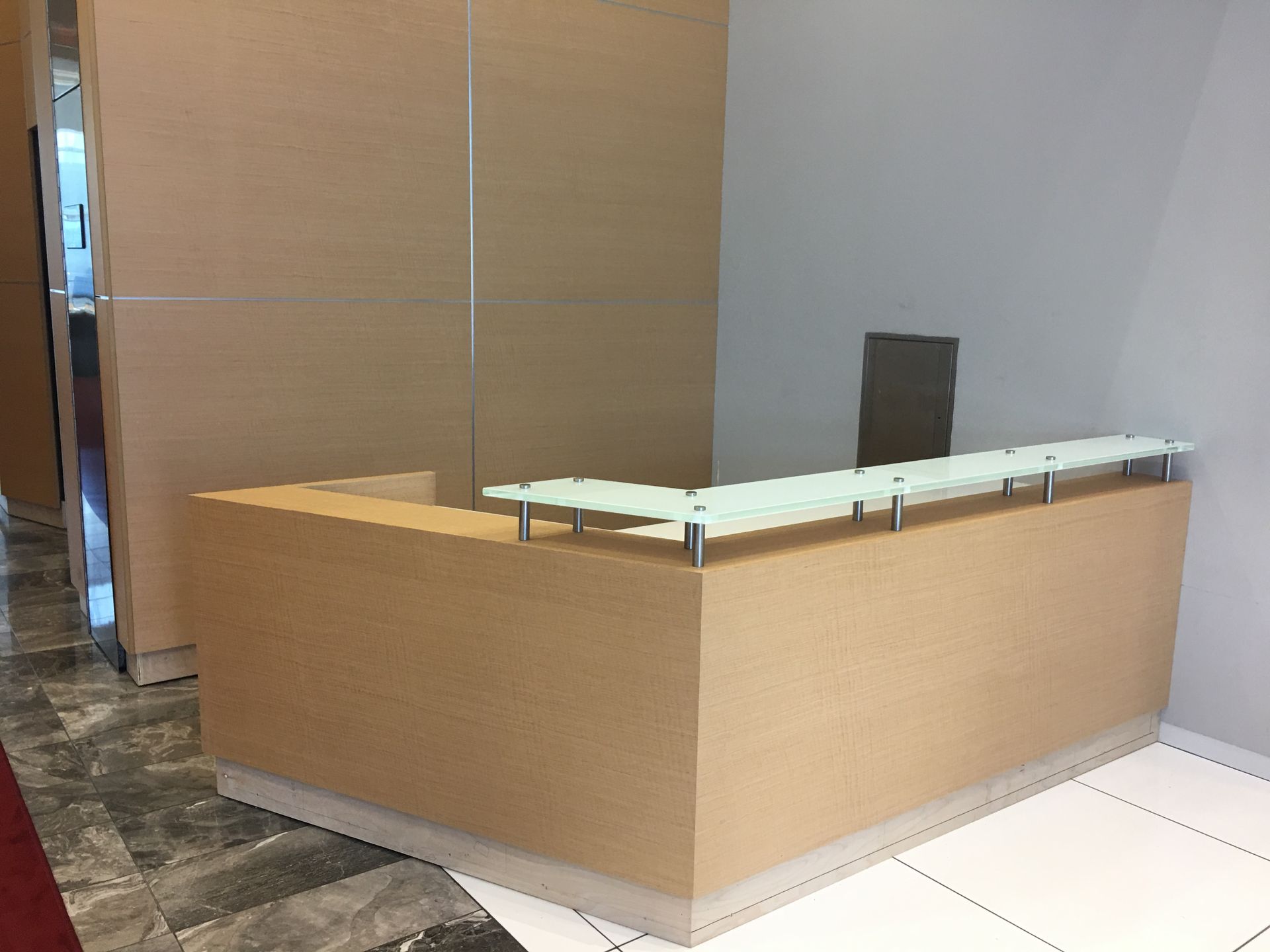 Beige reception desk with frosted glass top, set in a light-colored office space.