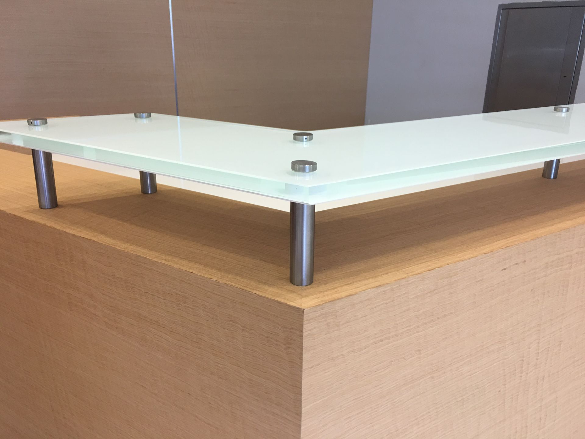 Corner desk with a glass top supported by metal legs on a light wood cabinet.