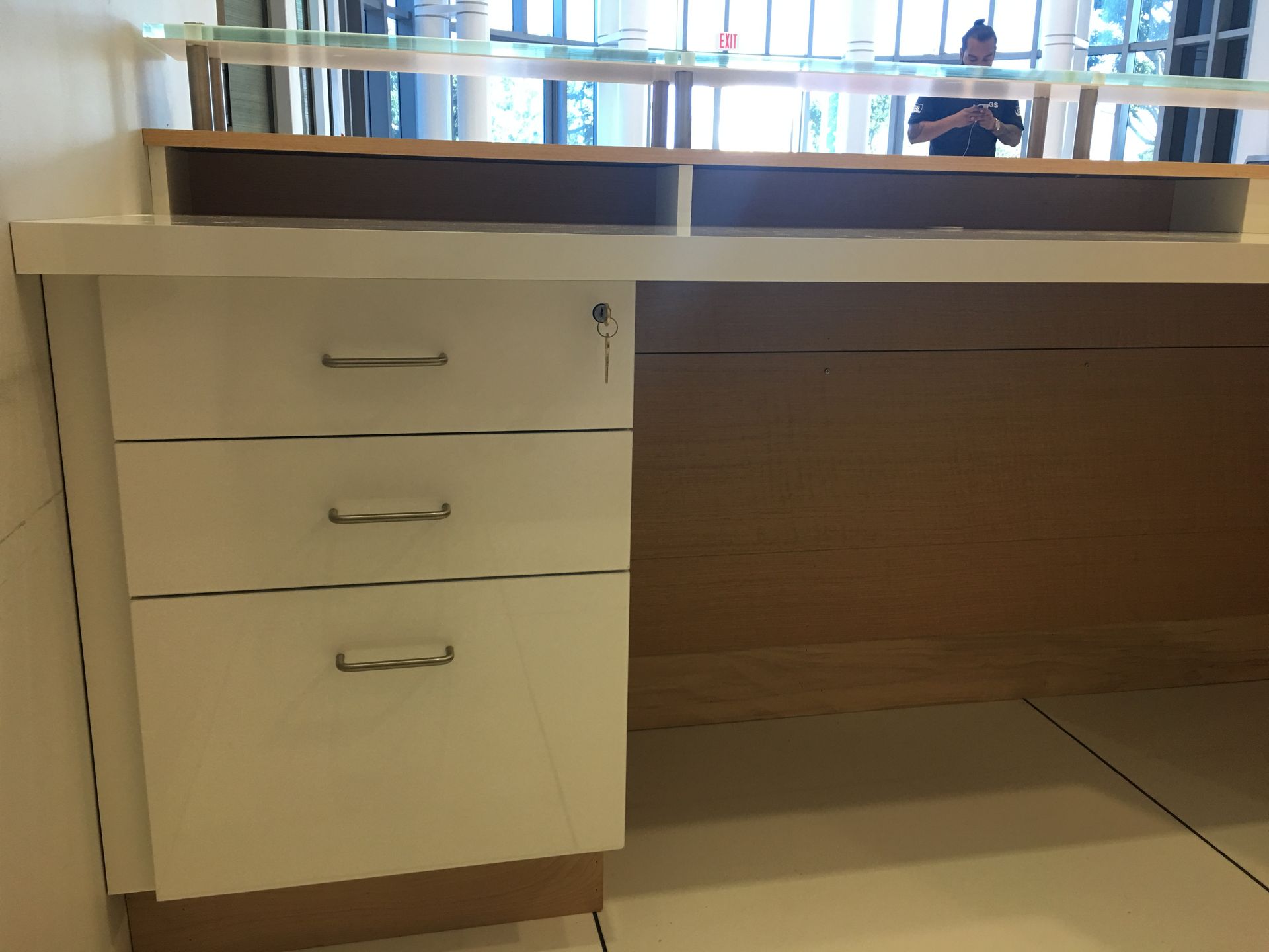 White desk with three drawers, key lock, and a person in the background.