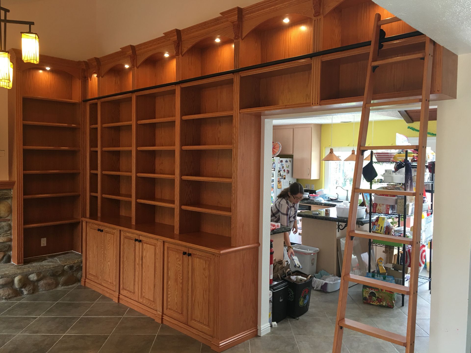 Wooden bookshelves built into a wall, with a person and a ladder in the doorway.