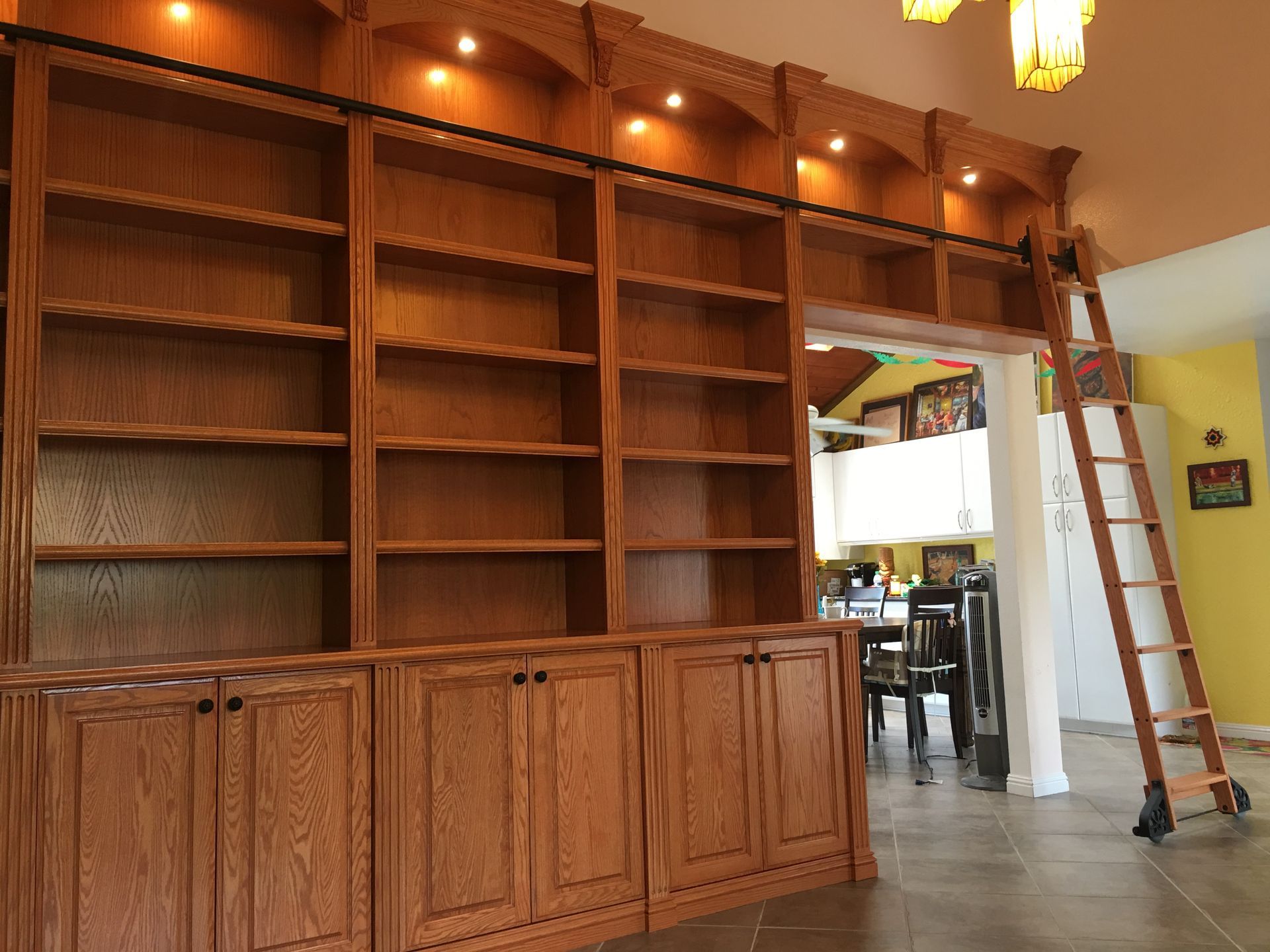 Wooden built-in bookcase with a rolling ladder. Includes cabinets, shelves, and recessed lighting.