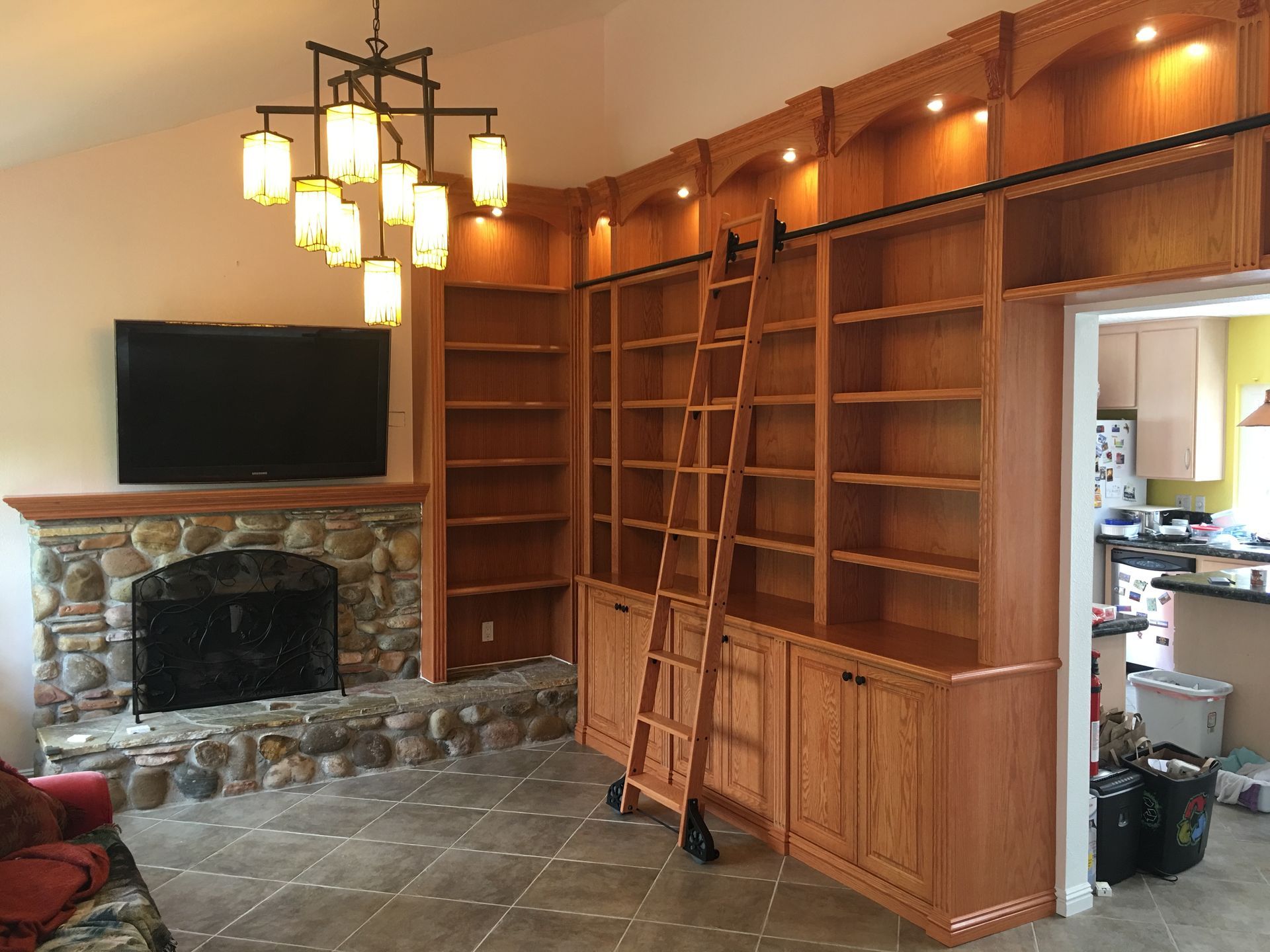 Living room with built-in bookshelves, ladder, fireplace, and television.