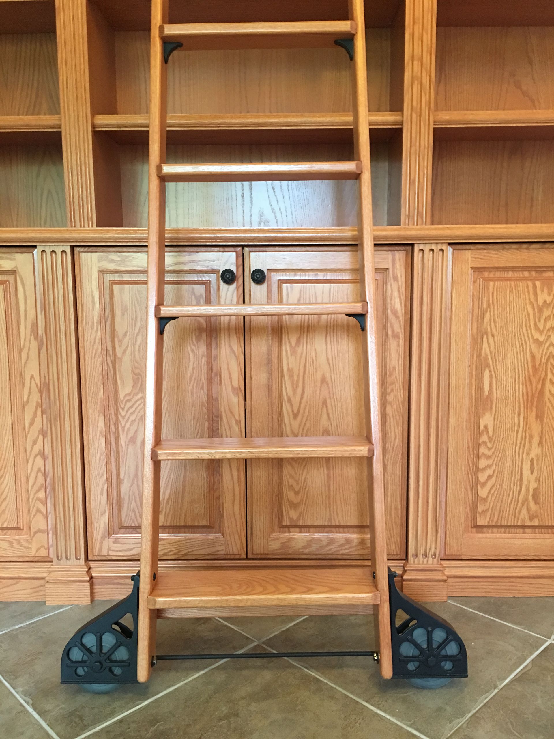 Wooden library ladder with black wheels, positioned in front of a wooden bookcase.