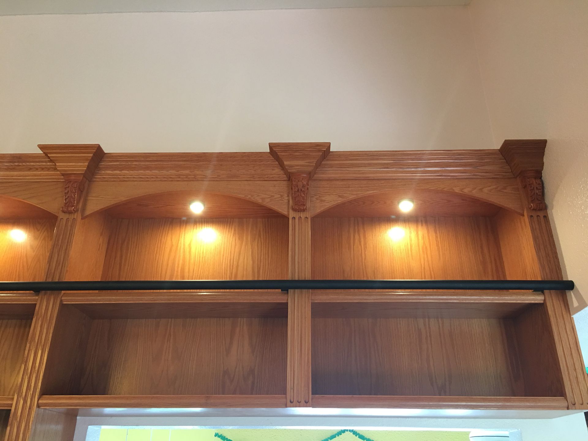 Wooden built-in shelf unit with arched top shelves, spotlights, and open bottom shelves; natural wood color.