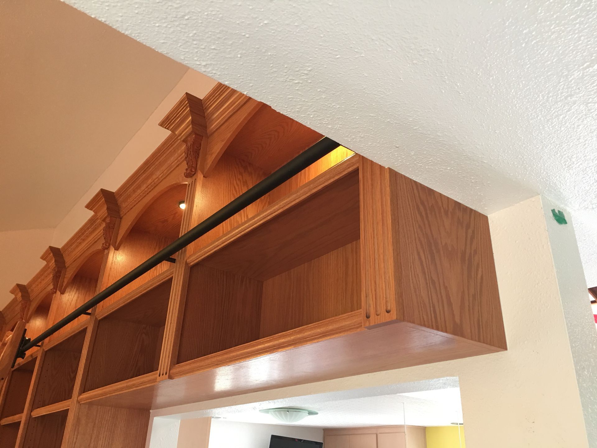Wooden cabinets with arched trim and black rod against a beige wall.