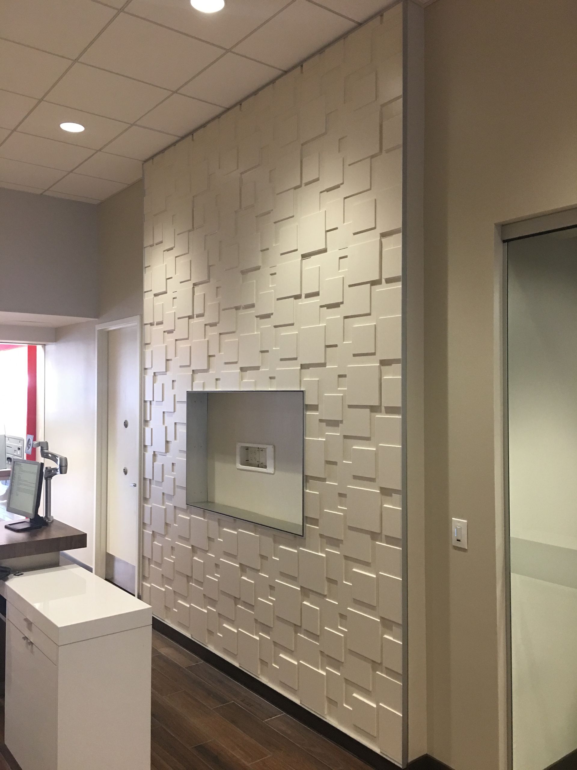 White, textured wall with recessed square pattern, built-in shelf, and adjacent white door.