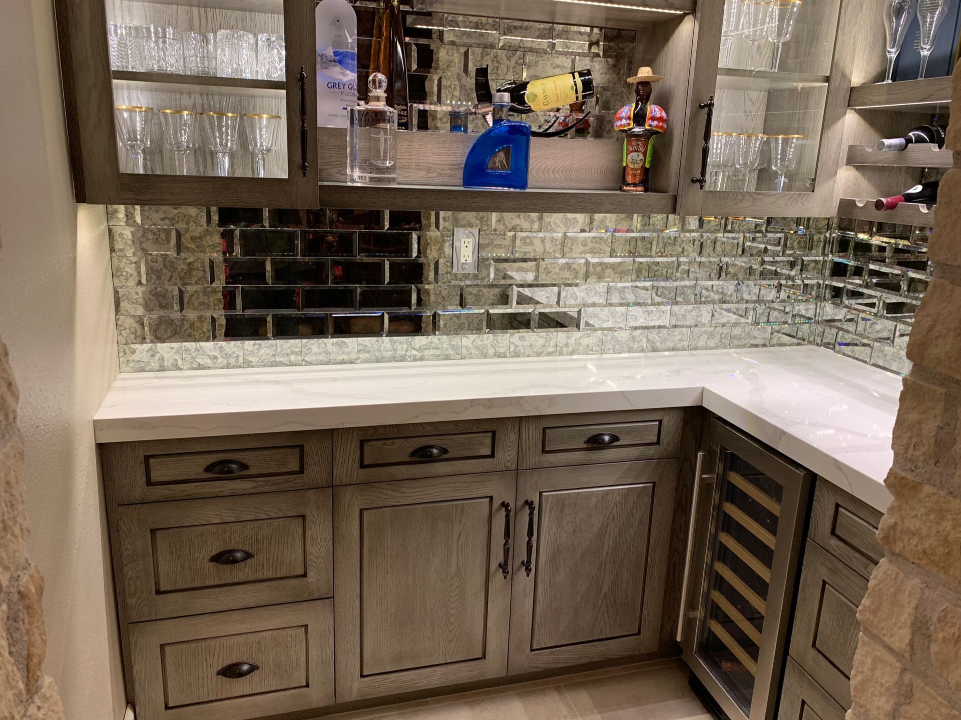 Built-in home bar with mirrored backsplash and upper cabinet with glassware, lower cabinet with wine fridge.