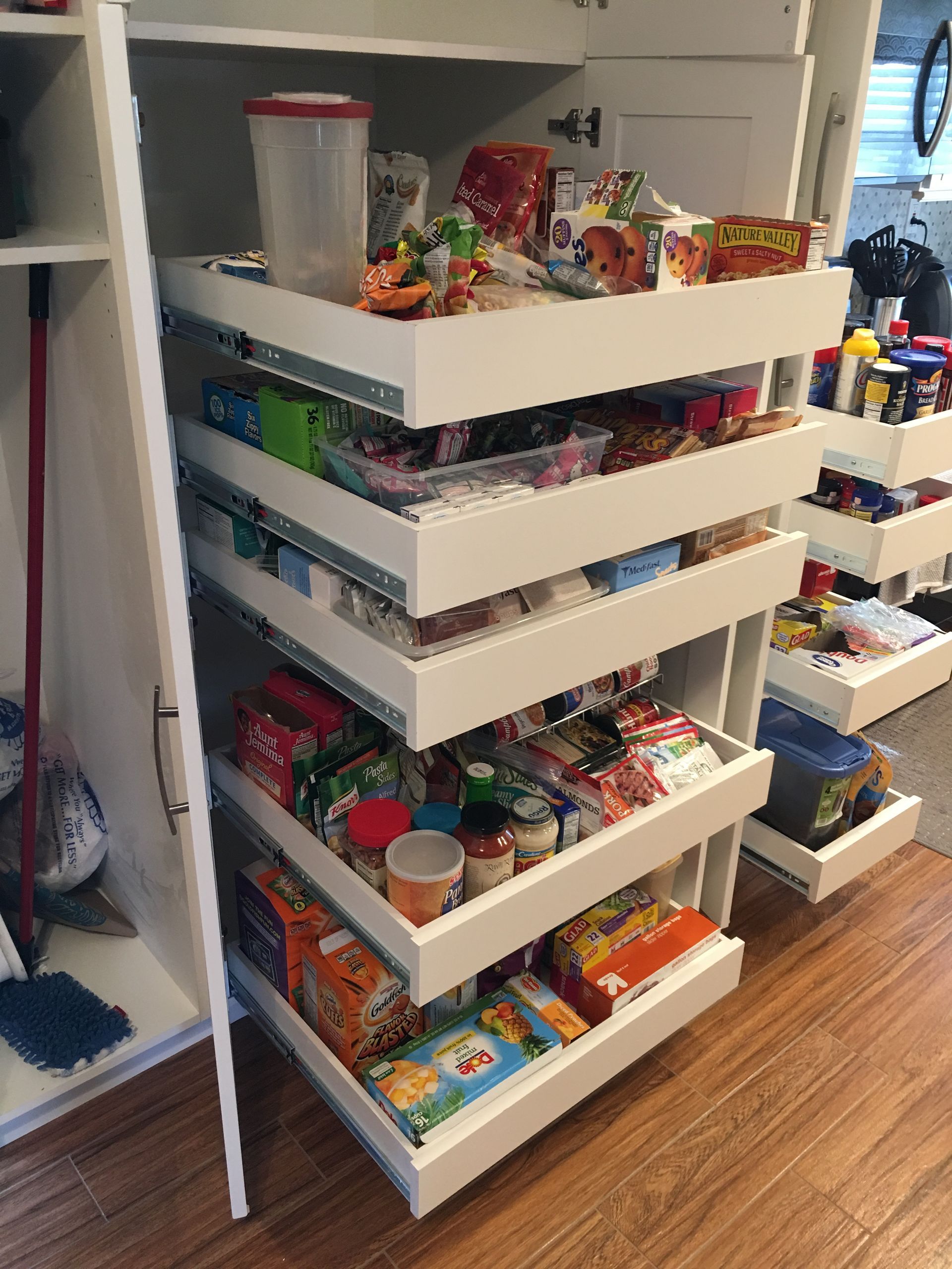 White pantry cabinet with pull-out shelves filled with various packaged food items.