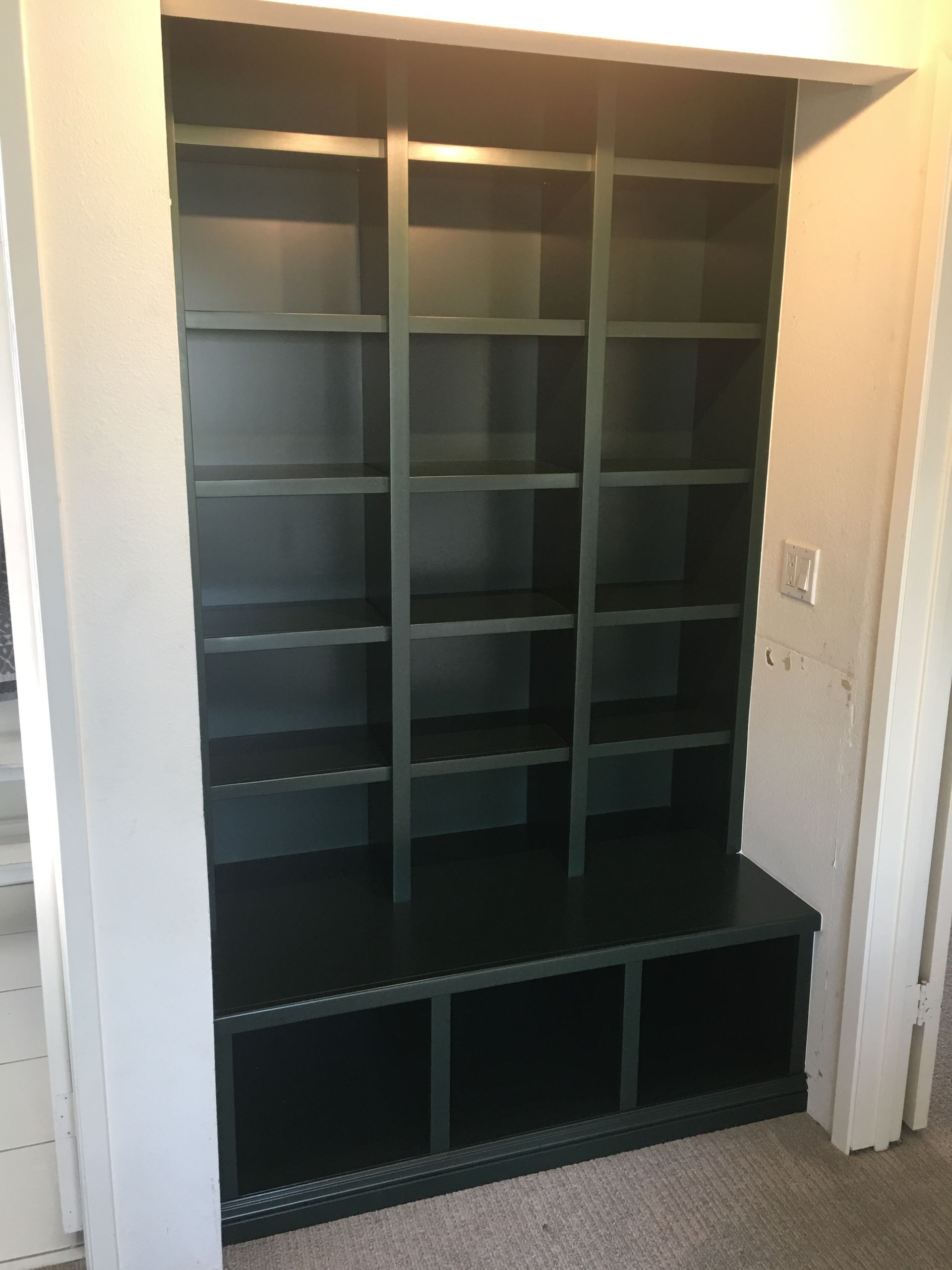 Built-in dark green storage unit with shelves and lower cabinet in a doorway.
