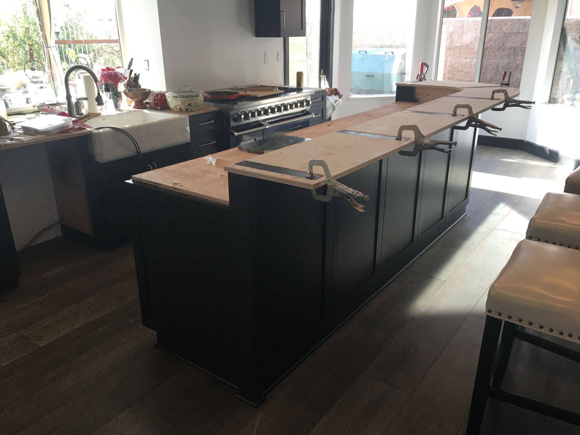 Black kitchen island with light wood countertop being installed, clamps holding it in place.