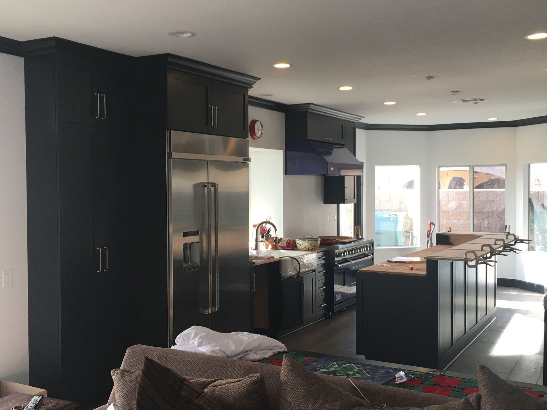 Kitchen with dark cabinets, stainless steel fridge, island with countertop, and windows.