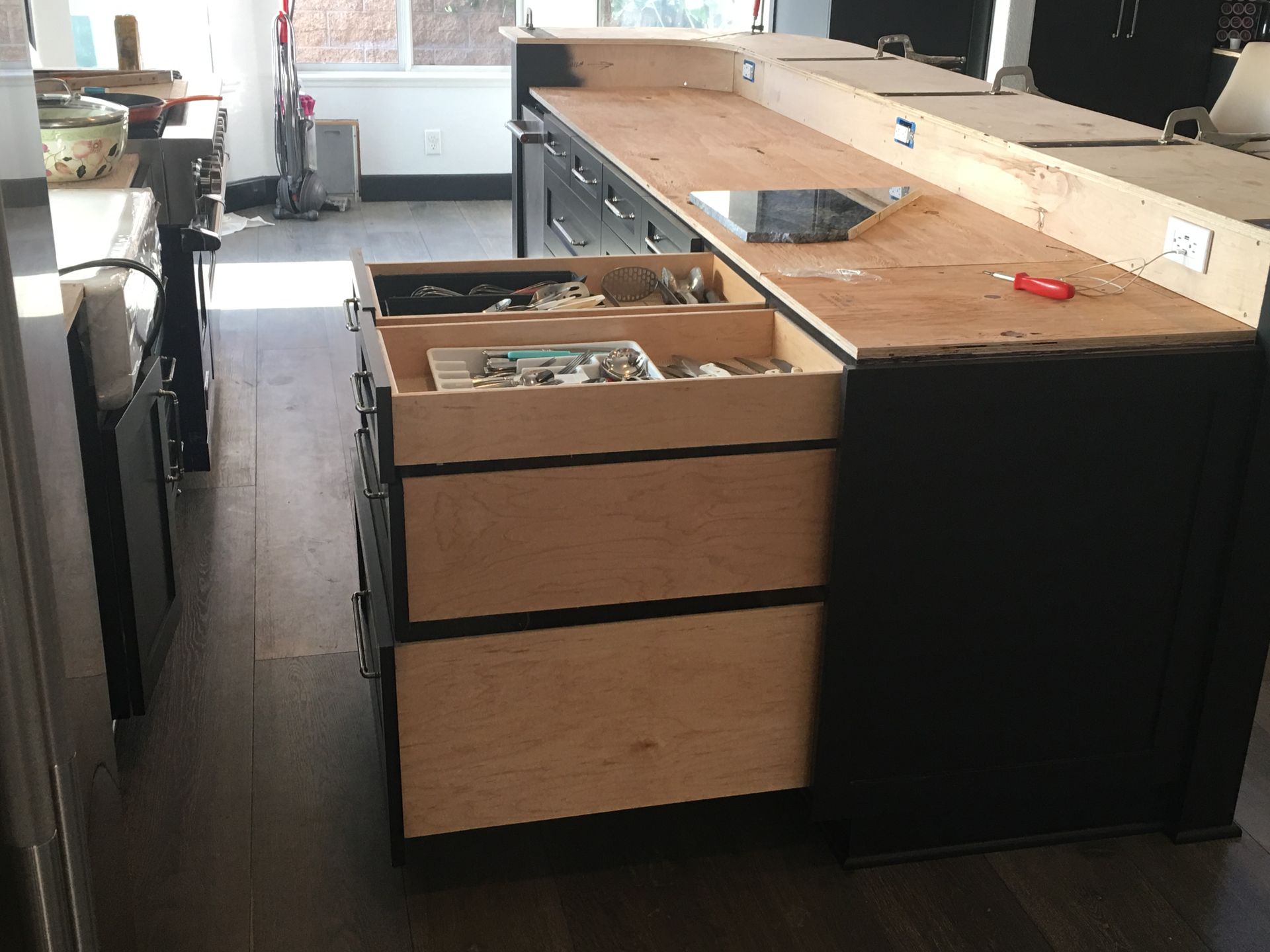 Kitchen island with open drawers, black cabinets, and wooden countertop.