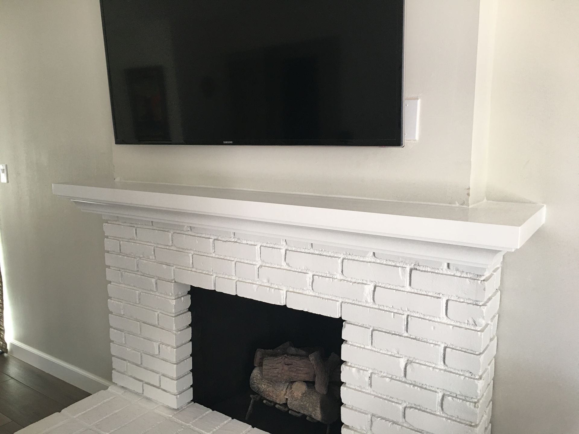 White painted brick fireplace with black insert, wood mantle, and TV mounted above.