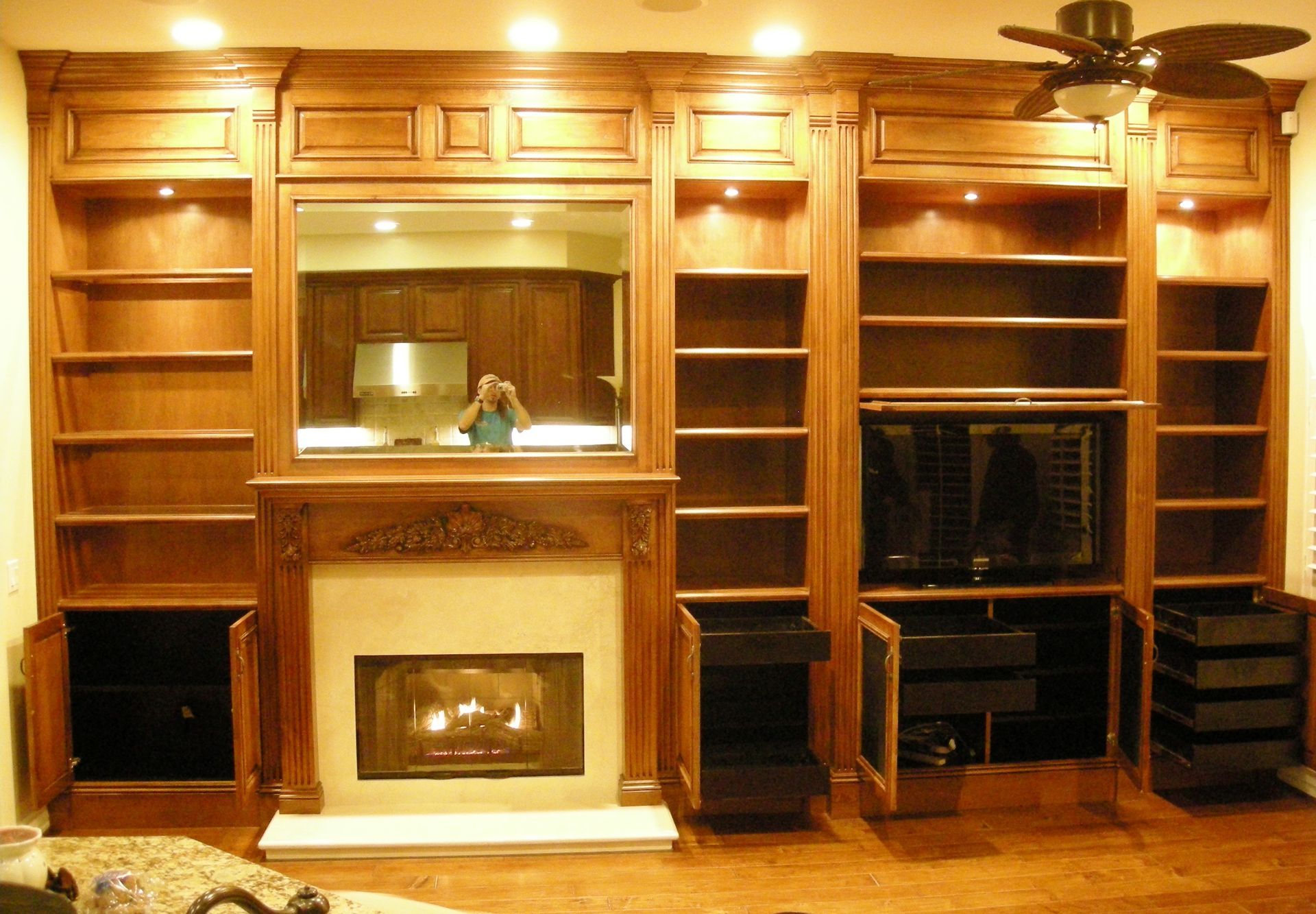 Wooden built-in shelving and fireplace with a mirror and television.