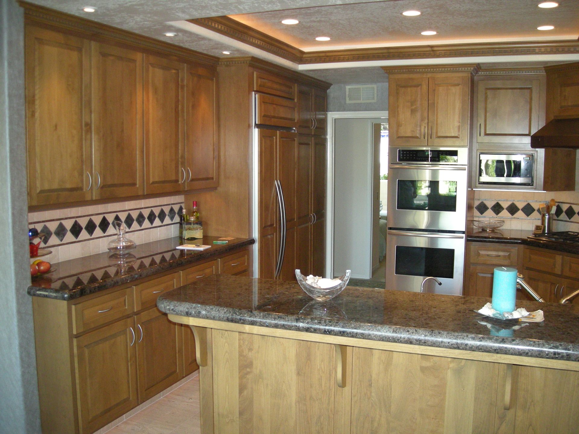 Kitchen with wood cabinets, granite countertops, and stainless steel appliances; open doorway in the background.
