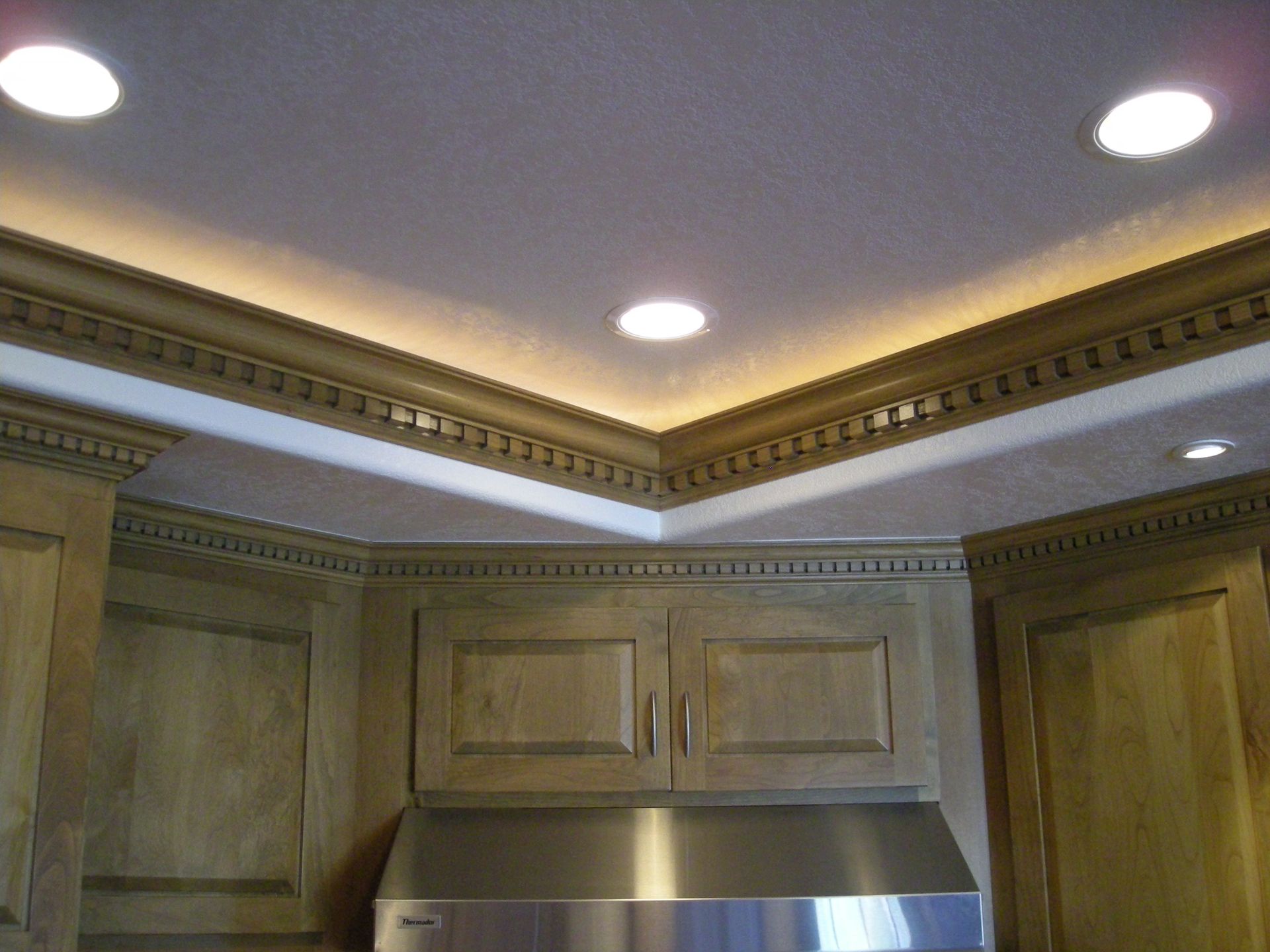 Kitchen cabinets with decorative crown molding and recessed lighting. Undercabinet range hood.