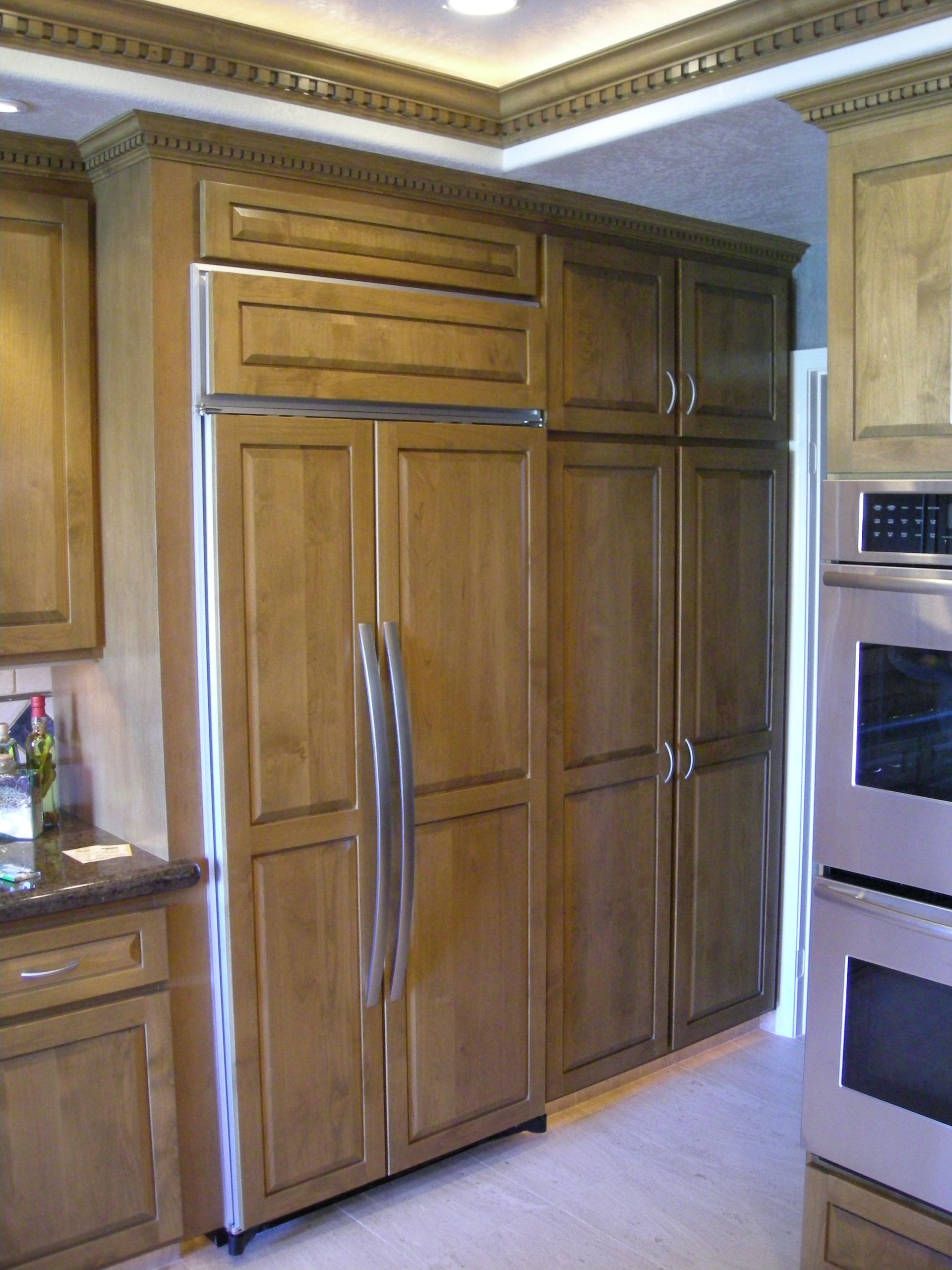 Wooden cabinetry with a refrigerator and pantry in a kitchen.