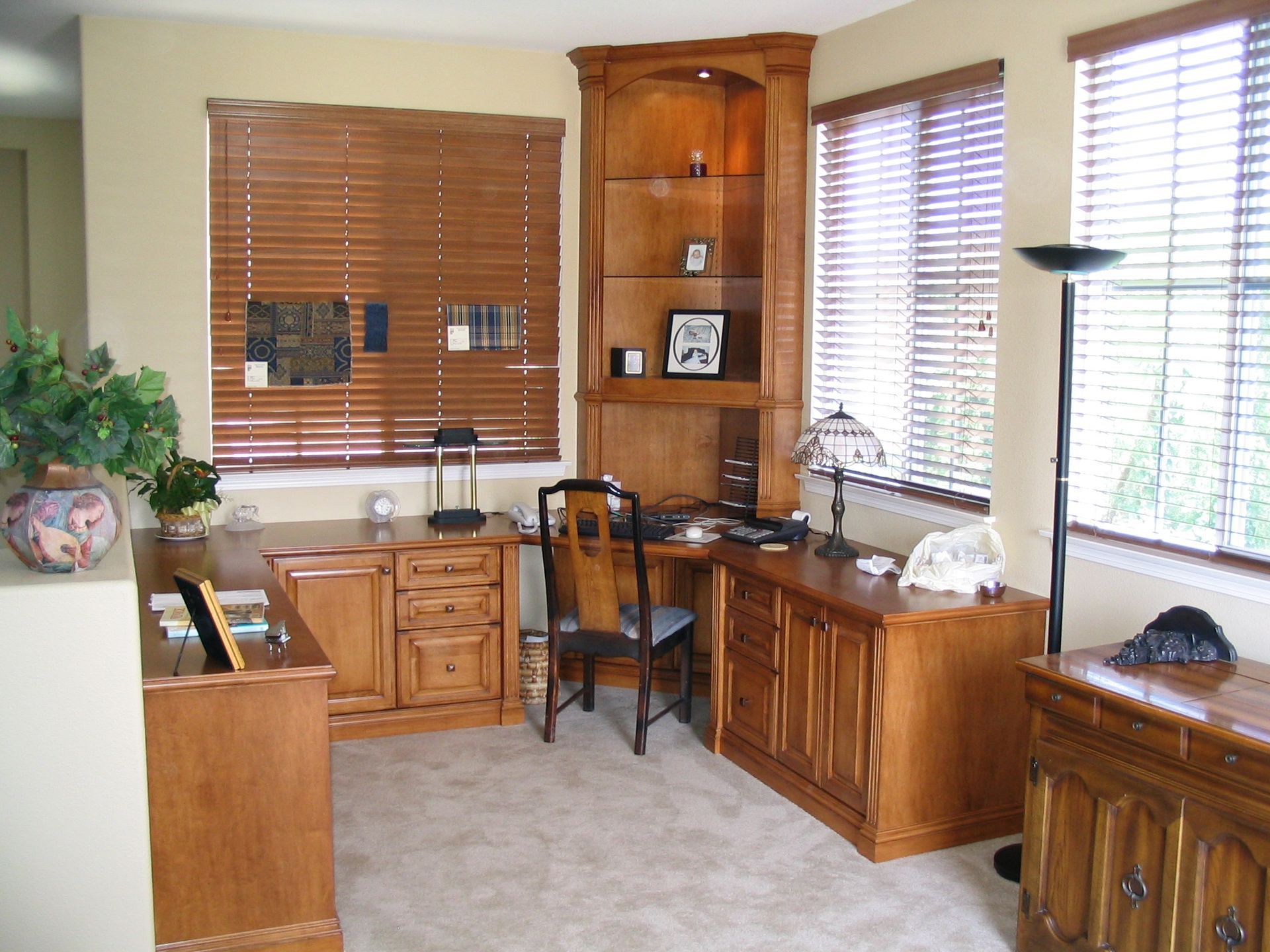 Corner office space with wooden desk, built-in shelving, and two shuttered windows.