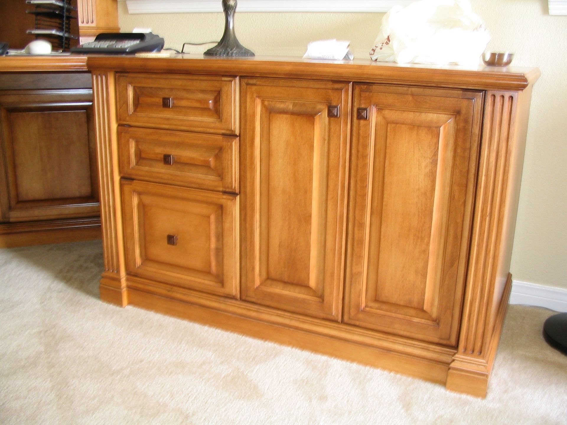 Wooden cabinet with three drawers and two doors, in a room with light carpet.