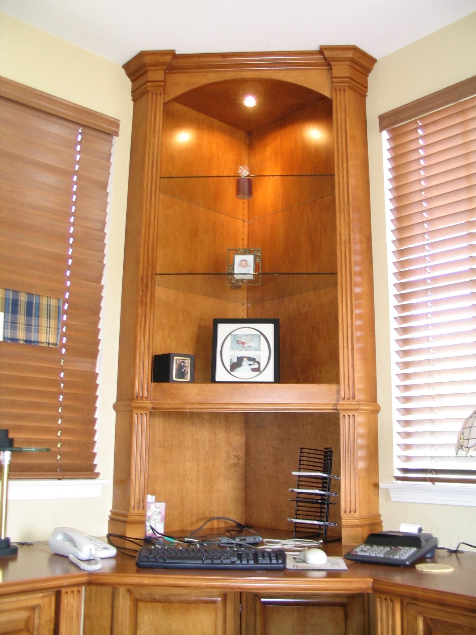 Corner built-in wooden cabinet with interior shelves and desk. Contains objects and is lit from within.