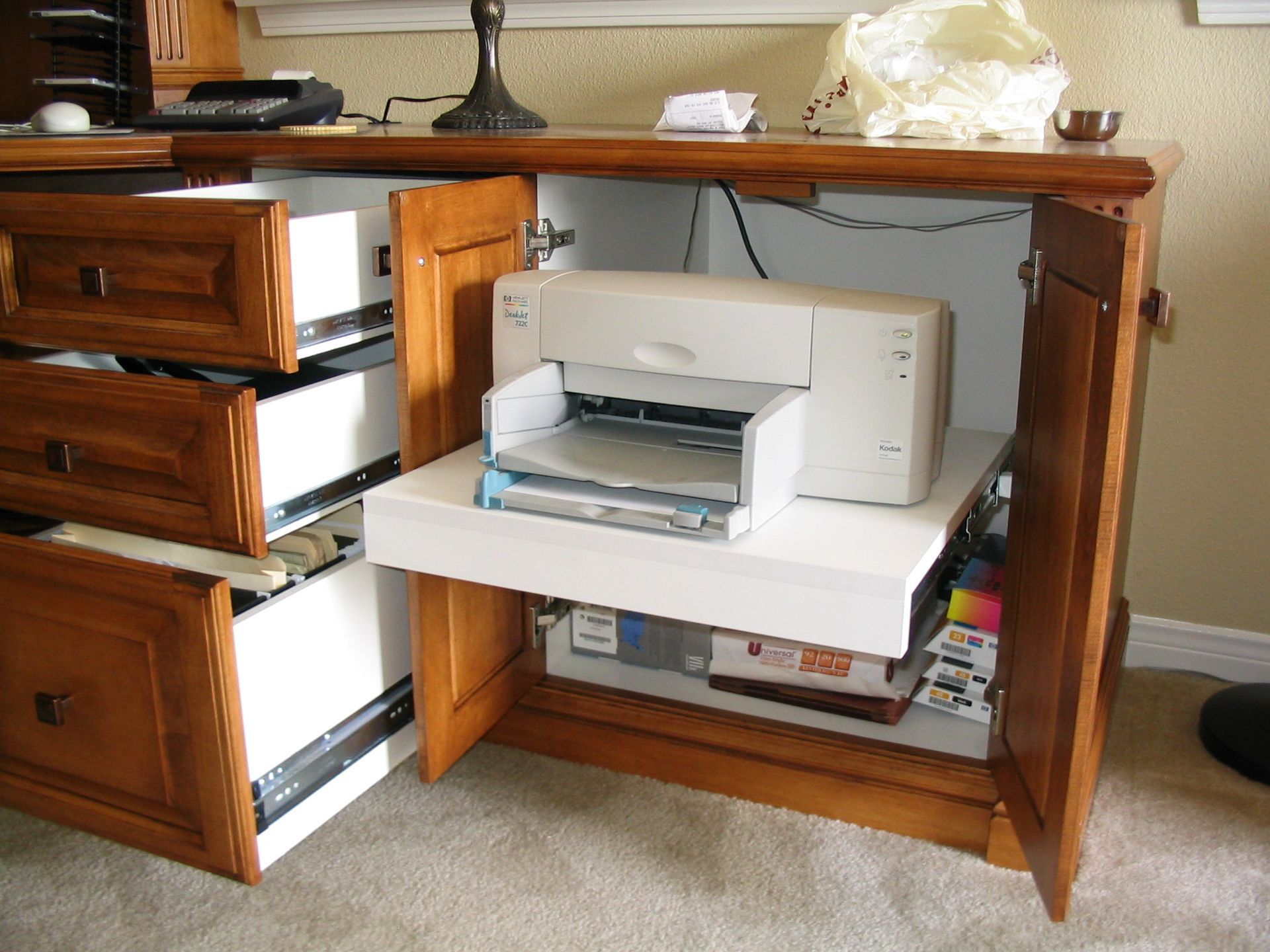 Wooden cabinet with open doors revealing a printer on a shelf and file drawers, office setting.