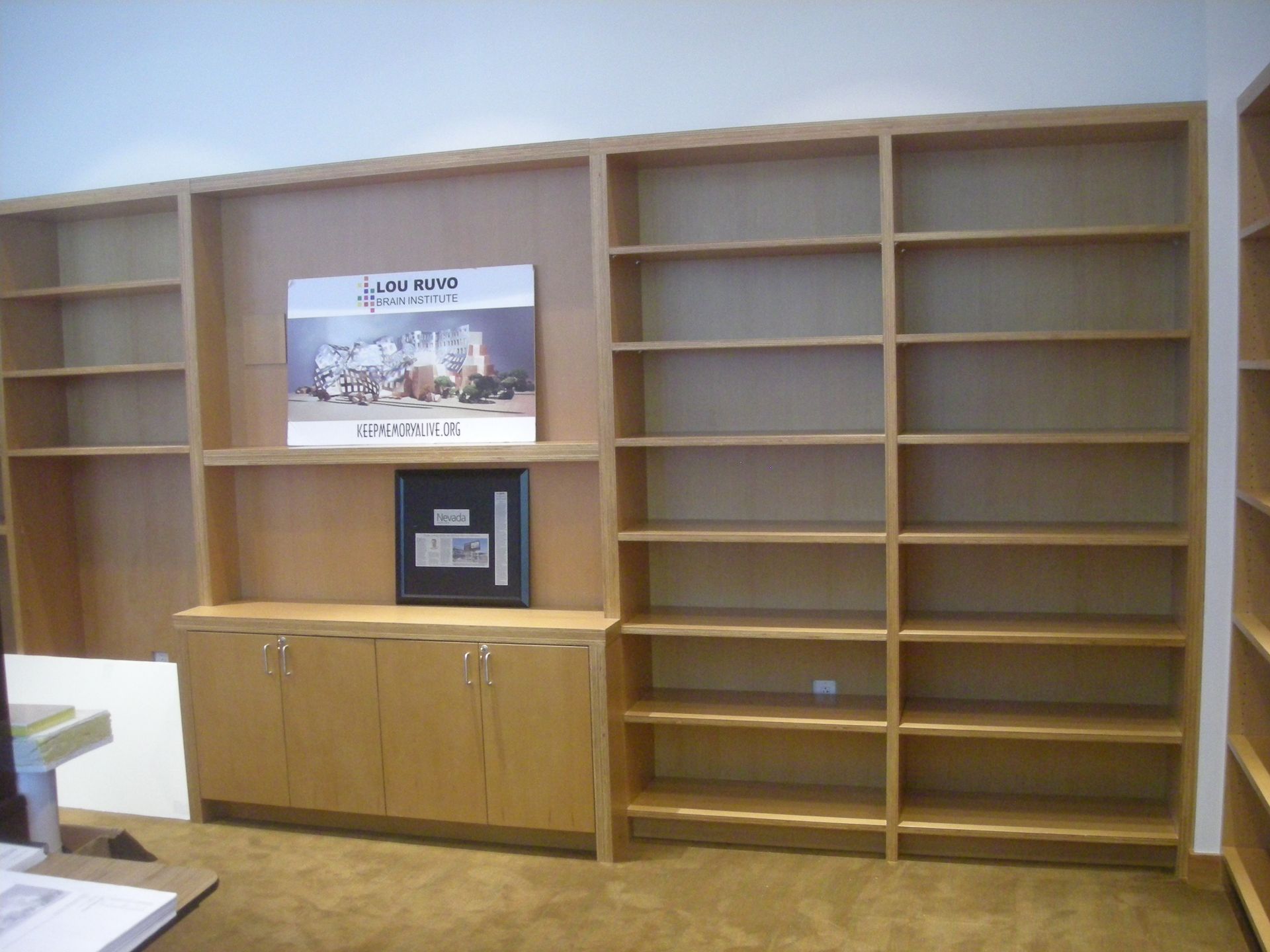 Empty wooden bookshelves against a wall. A cabinet is in the lower section of shelves.