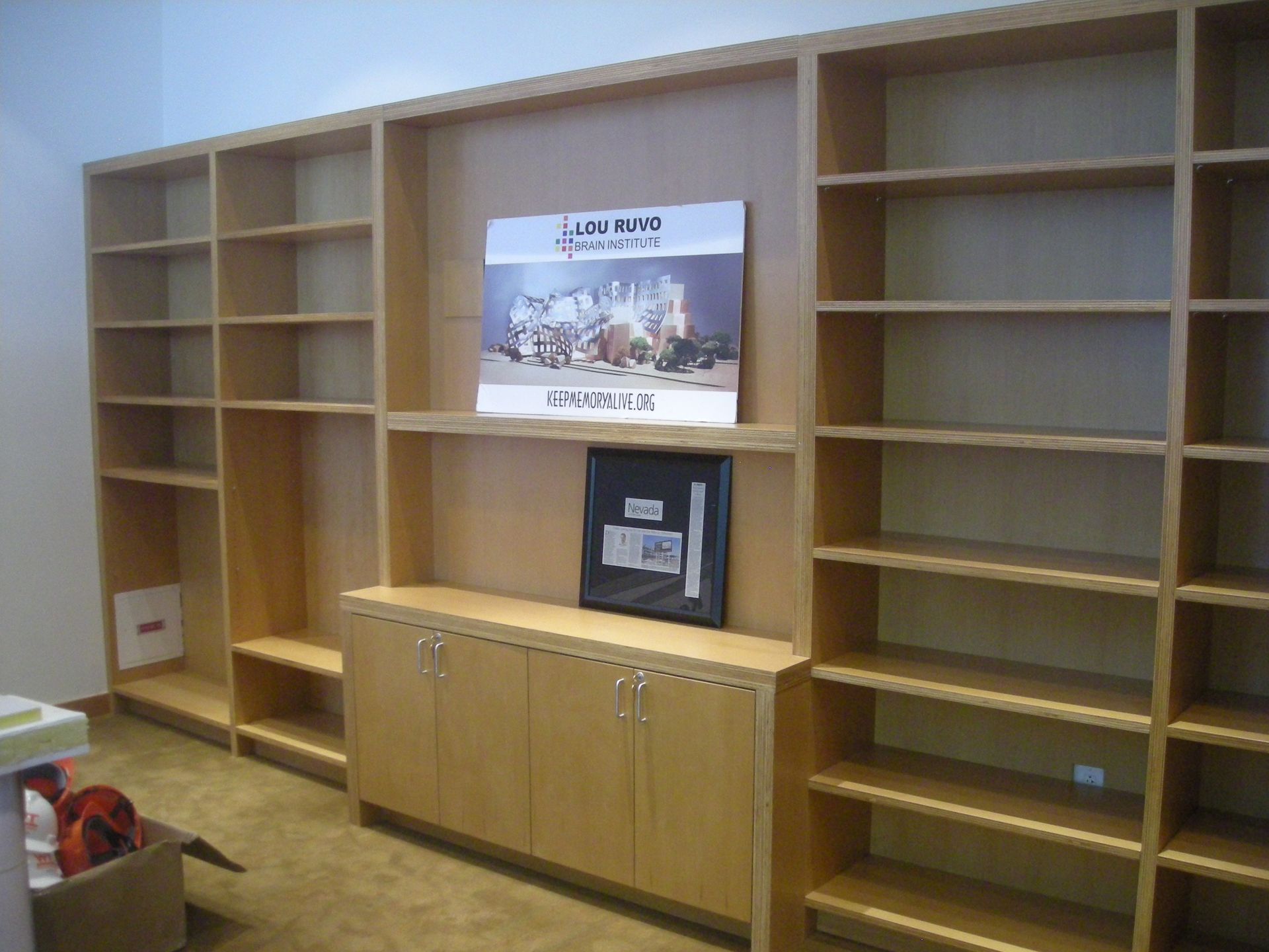 Built-in wooden shelves and cabinets against a neutral wall; a framed document and poster are displayed.