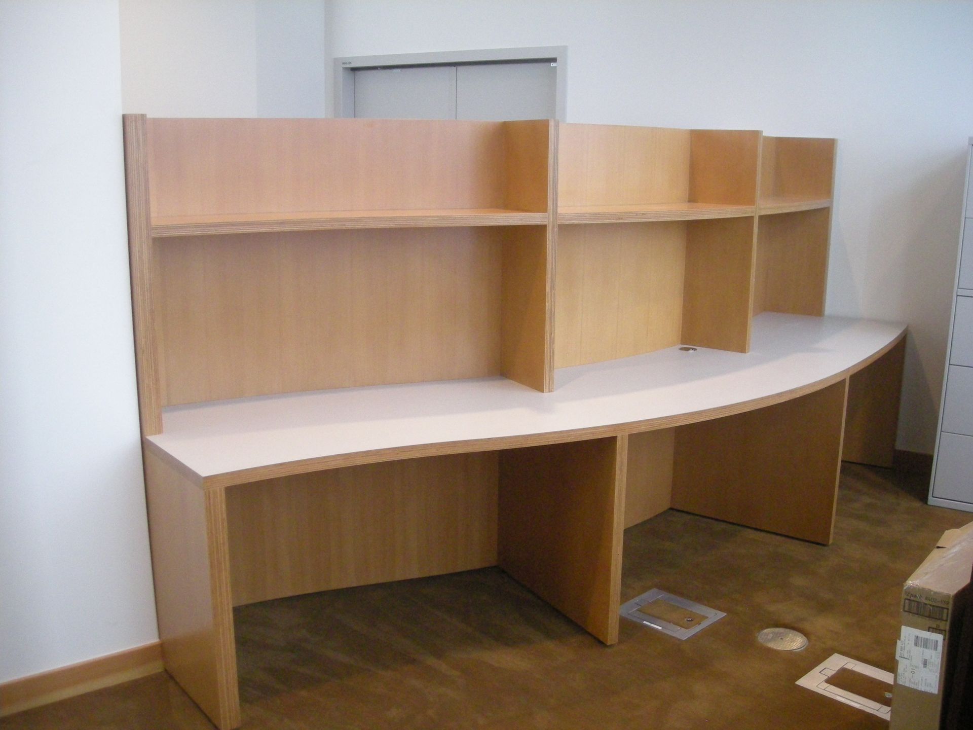 Light wood office cubicle with shelves and curved desk surface.