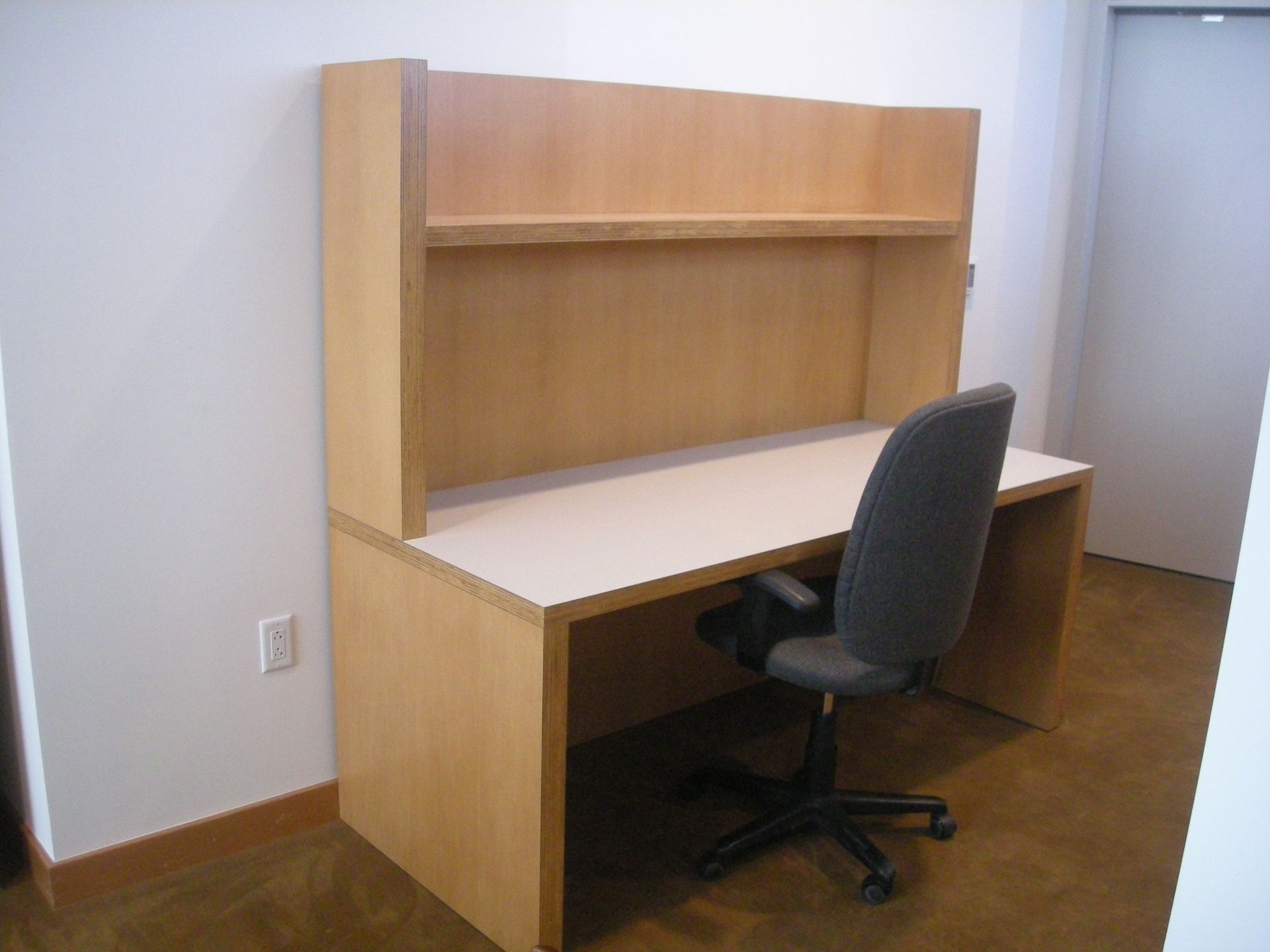 Desk with a light wood finish, integrated hutch, and a gray office chair in a room.