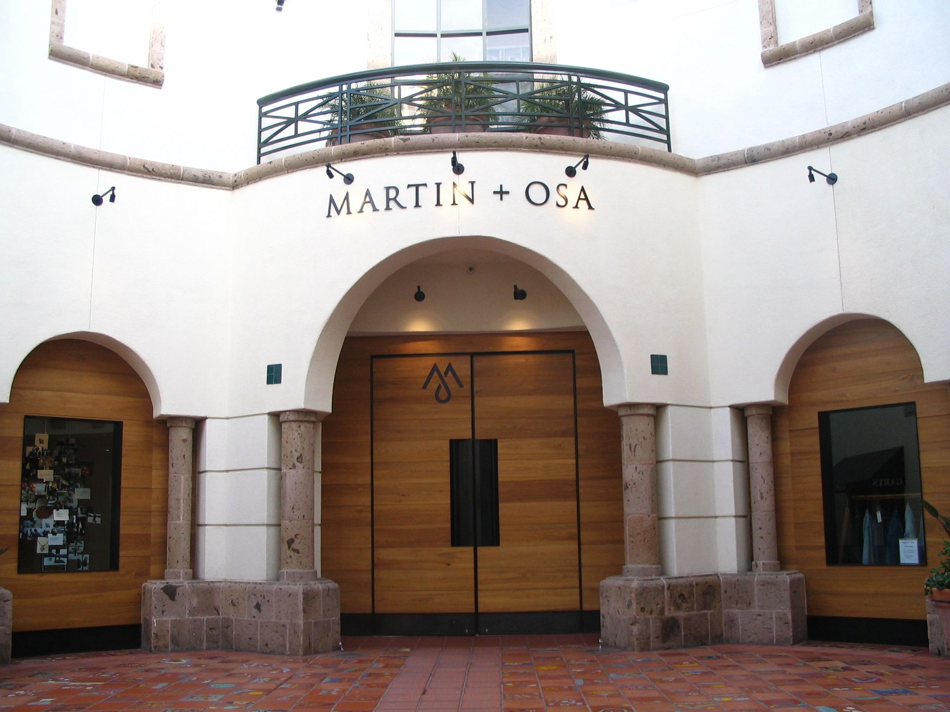 Exterior of a Martin + Osa store with arched entrance, large wooden doors, and decorative balcony.