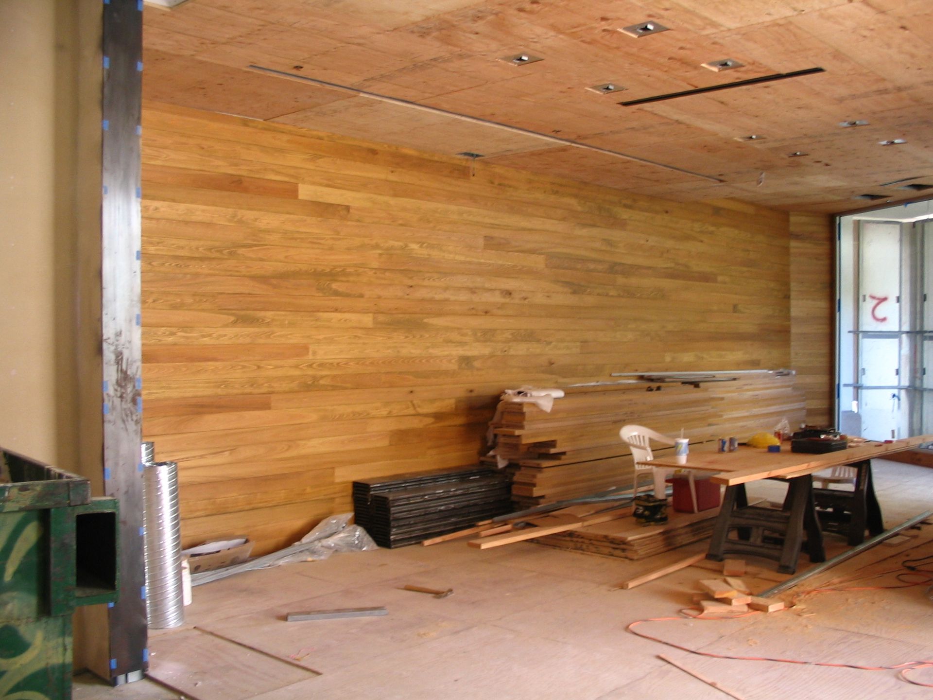 Interior construction with wood paneling on walls. Tools and materials are scattered around the space.