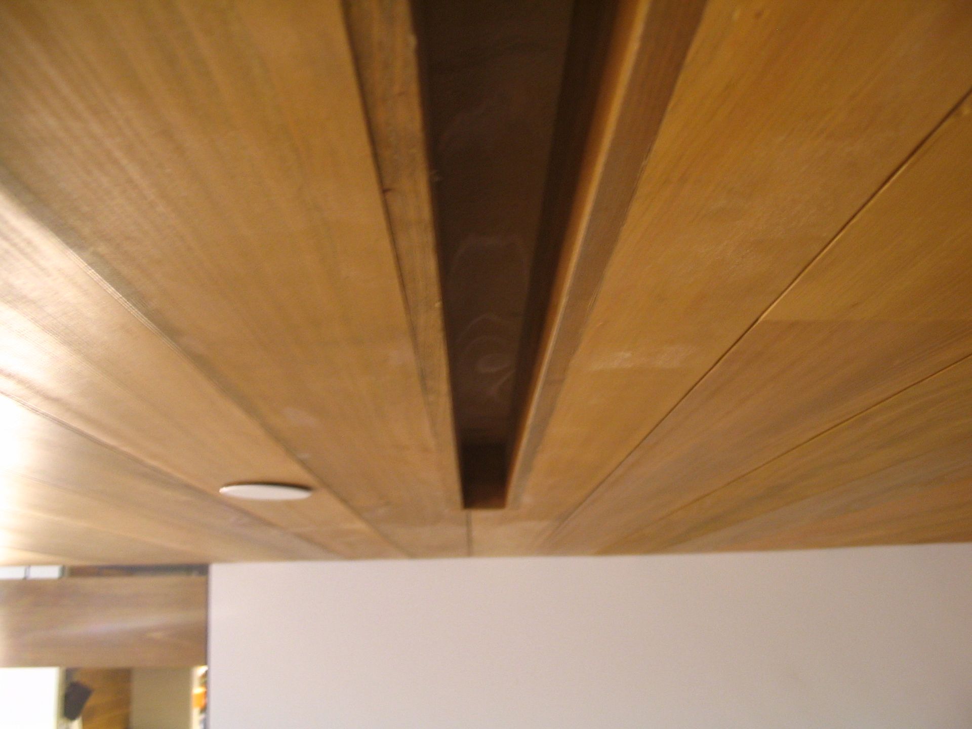 Wooden ceiling with recessed channel and a white wall below.