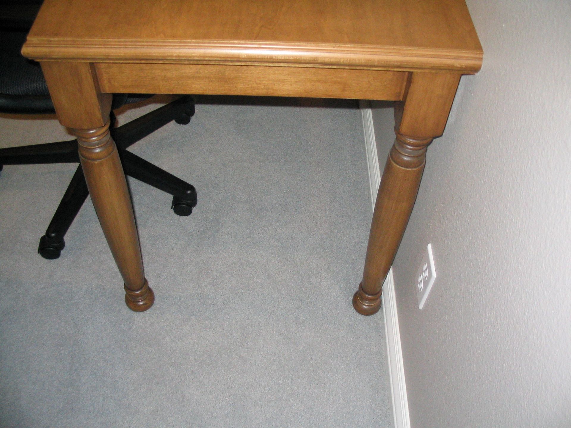 Wooden side table with turned legs, set on gray carpet next to a wall.