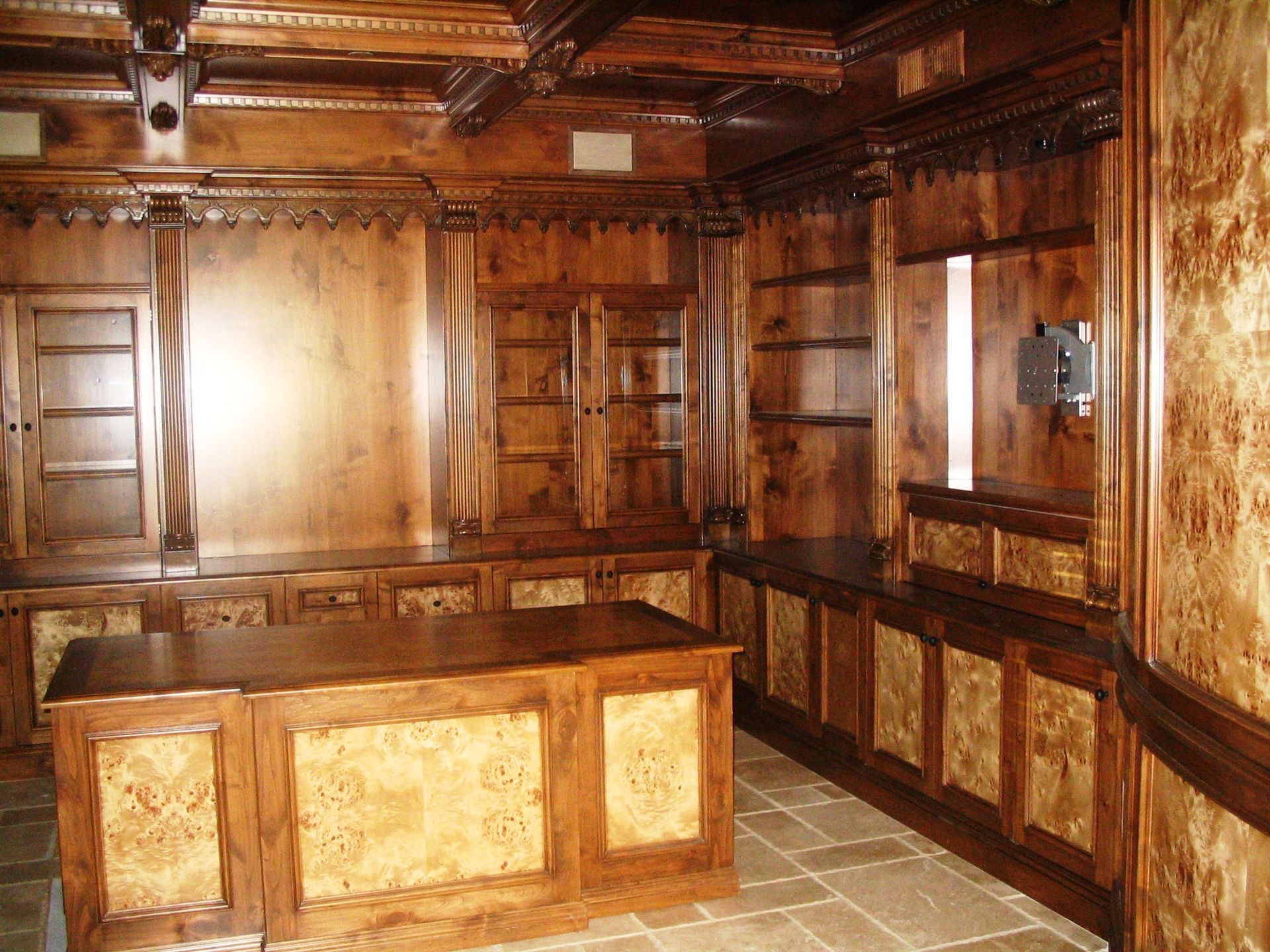 Ornate wood-paneled room with built-in desk, shelves, and ornate ceiling details. Light and dark wood tones.
